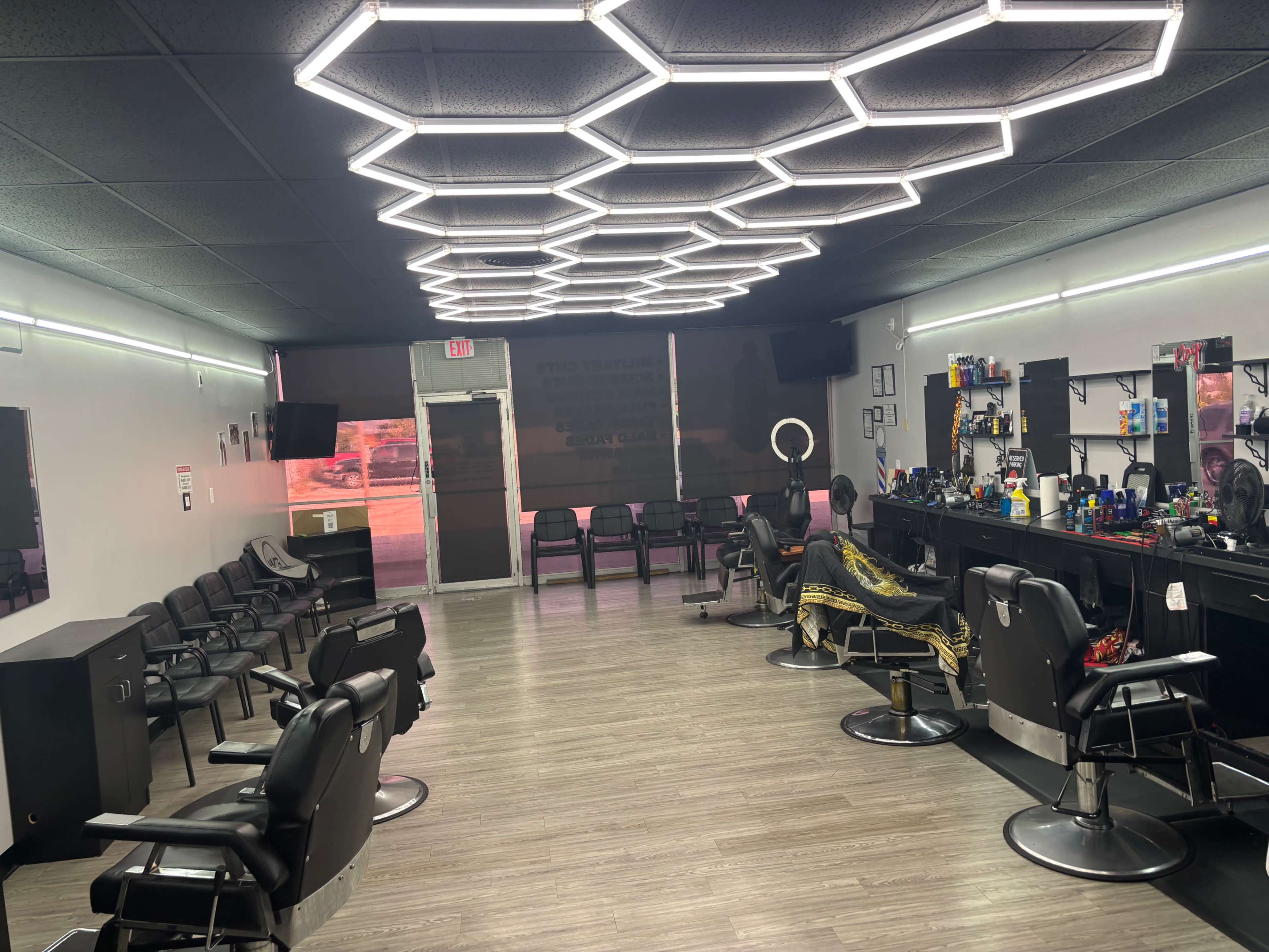 The image shows the interior of a modern barbershop with several styling chairs, a mirror-lined counter, and hexagonal lighting fixtures on the ceiling.