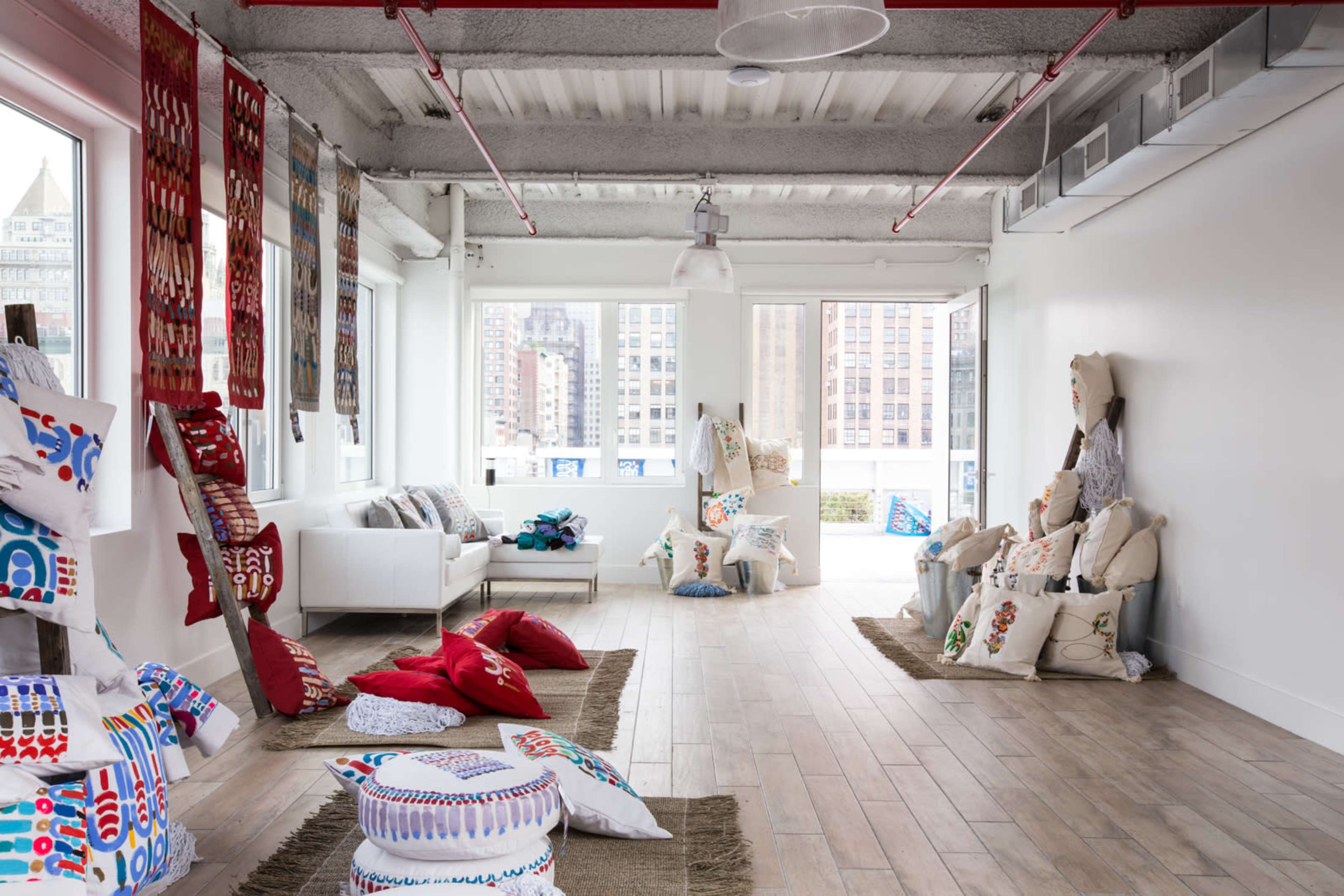 A spacious room filled with colorful pillows and decorative textiles, featuring large windows that allow natural light to illuminate the space.