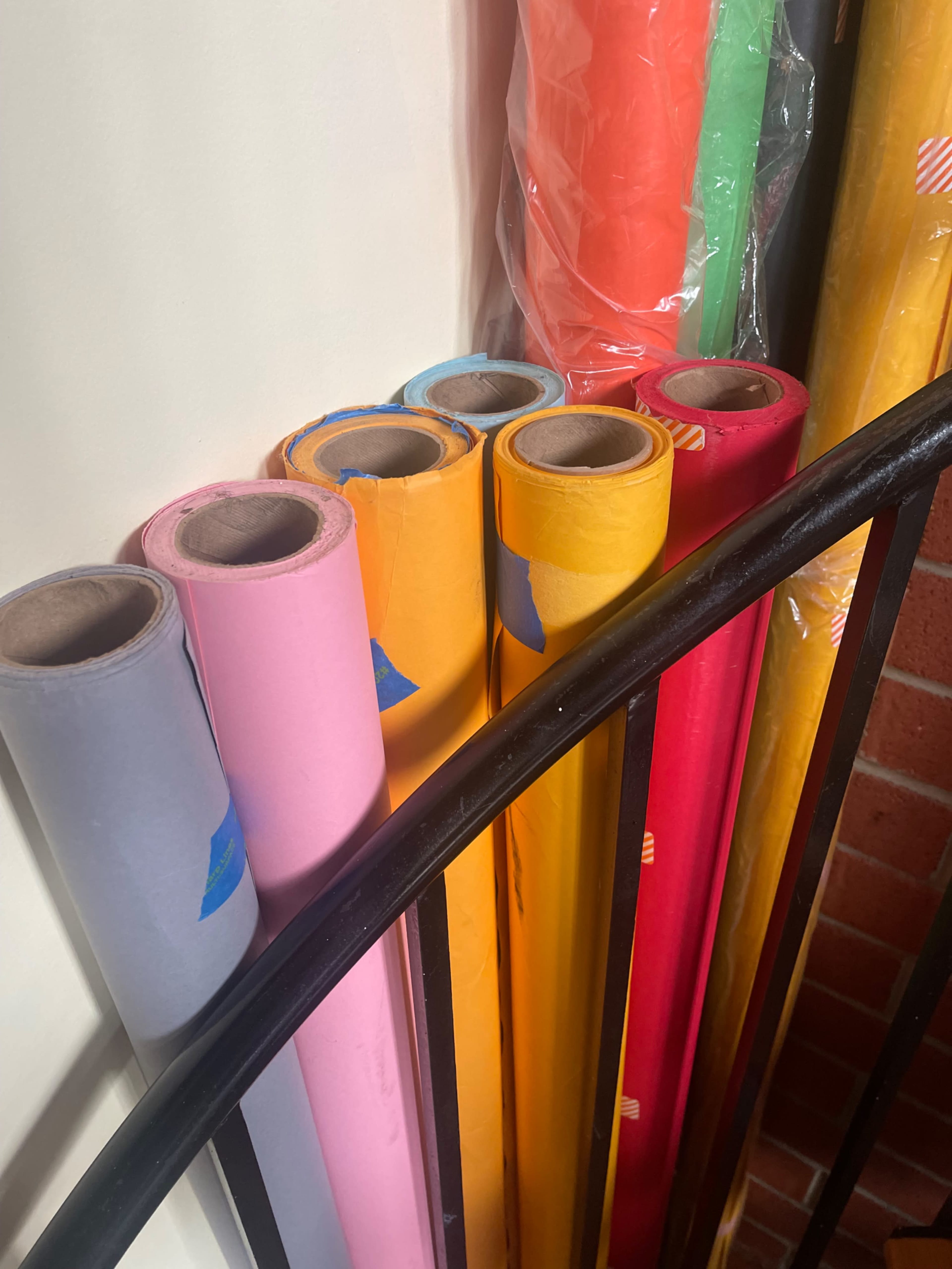 A collection of rolled paper in various colors, neatly arranged next to a black metal railing.