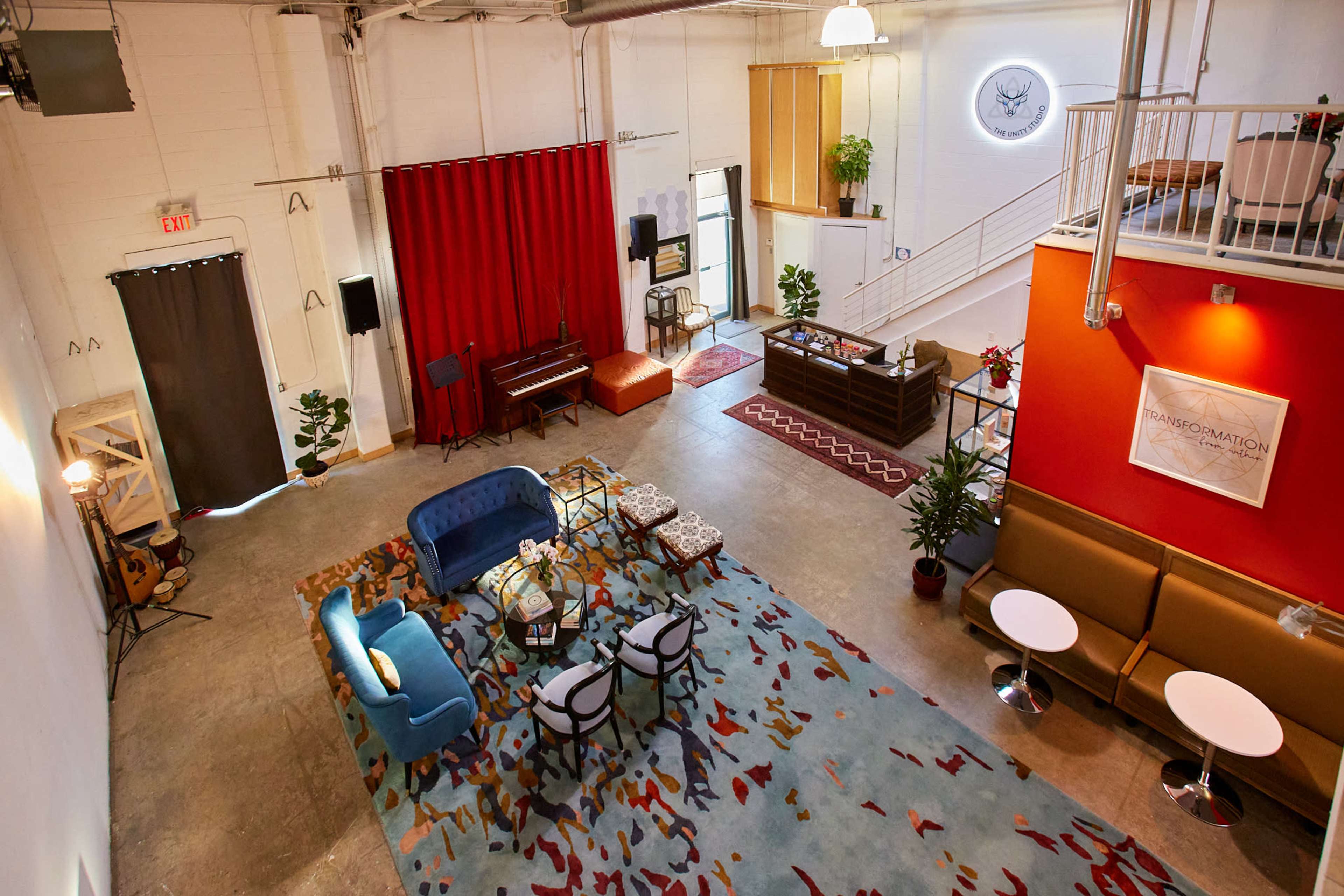 A spacious interior with a mix of seating areas, including a blue couch, chairs, and tables, alongside a piano and a reception area.