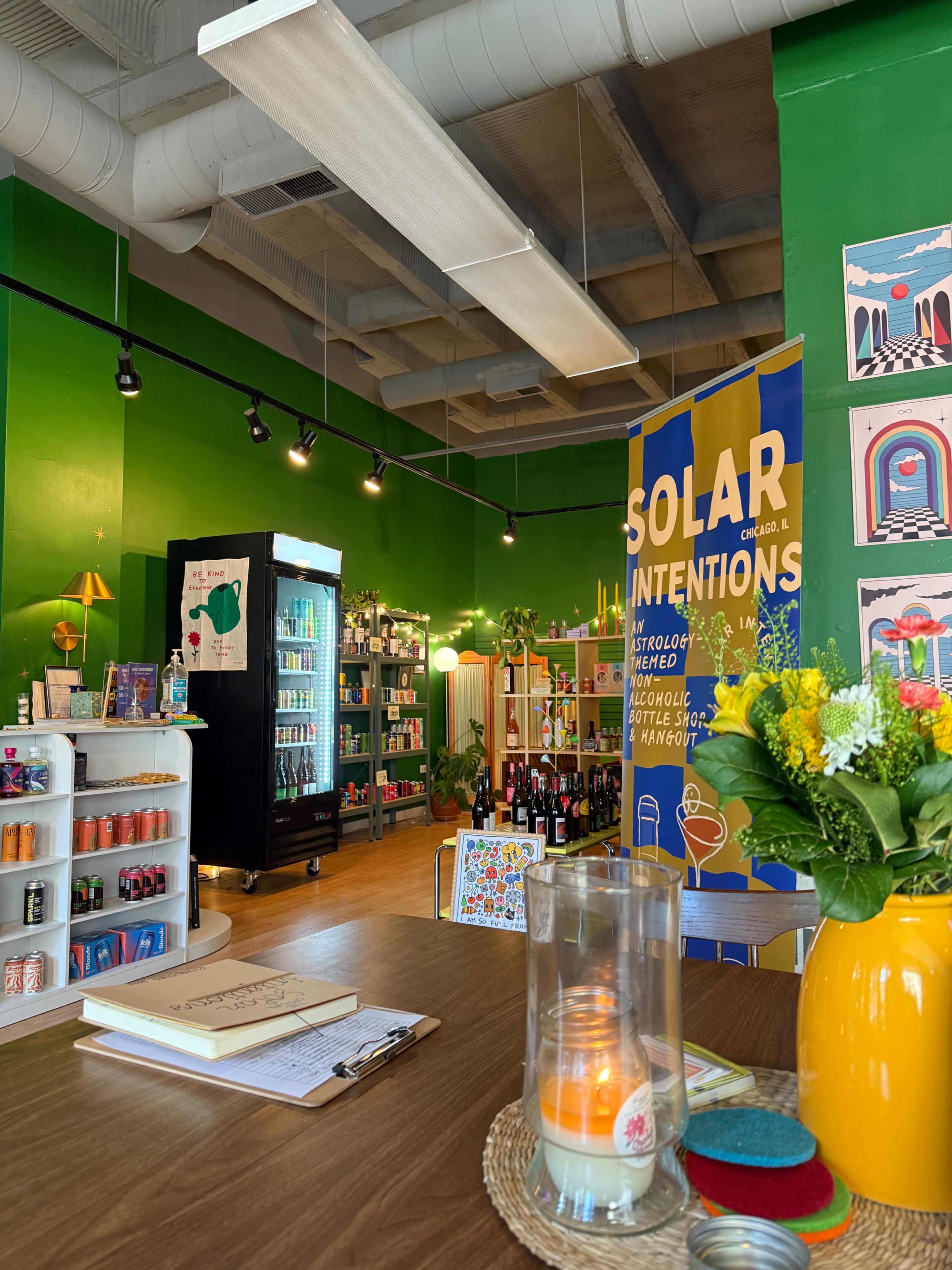 The image shows a vibrant green wall interior of a shop filled with shelves of various products, including beverages, and a brightly colored banner that reads "SOLAR INTENTIONS."