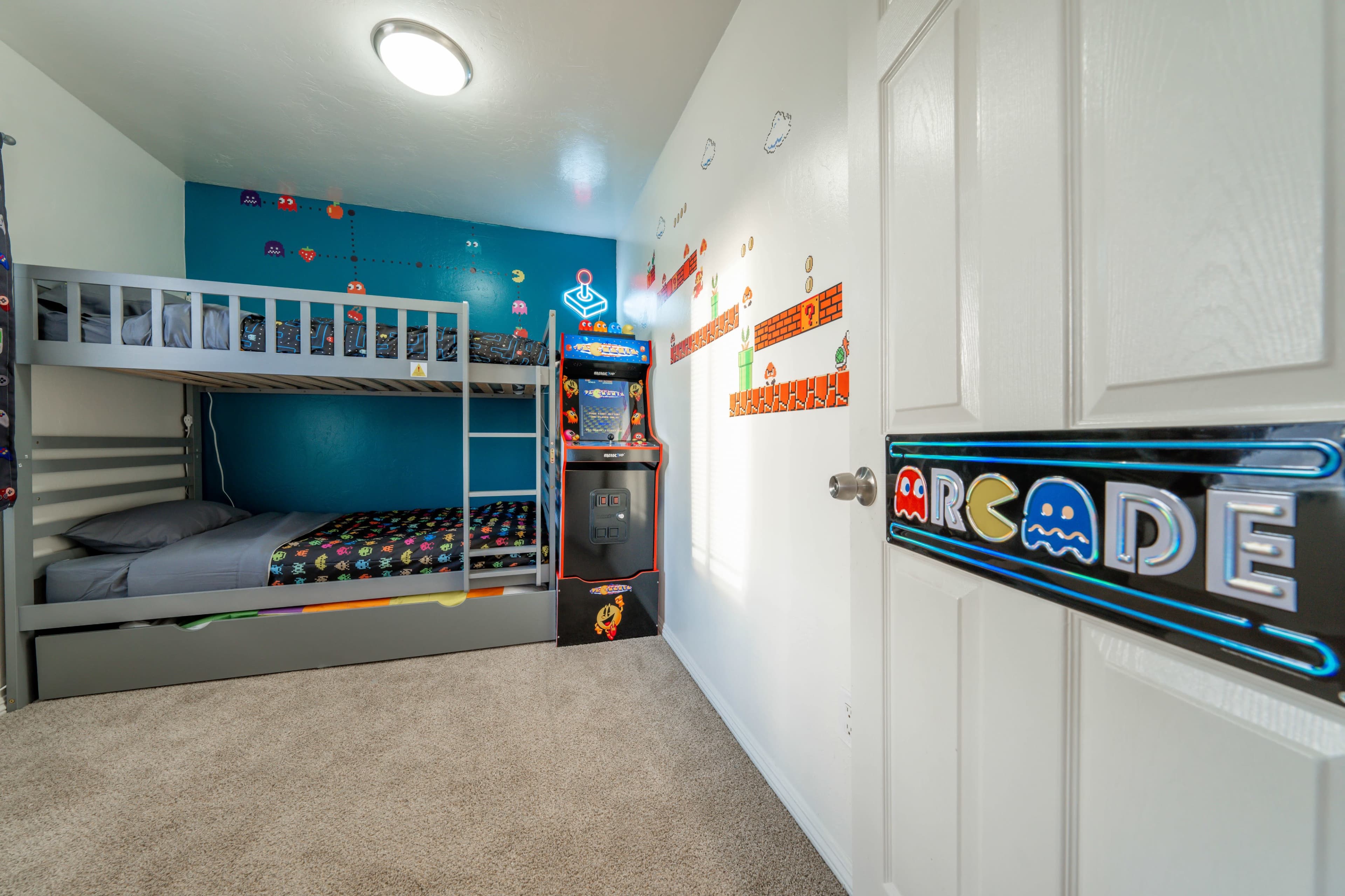 A child's bedroom featuring a lofted bed, game-themed decorations on the walls, and an arcade cabinet in one corner.