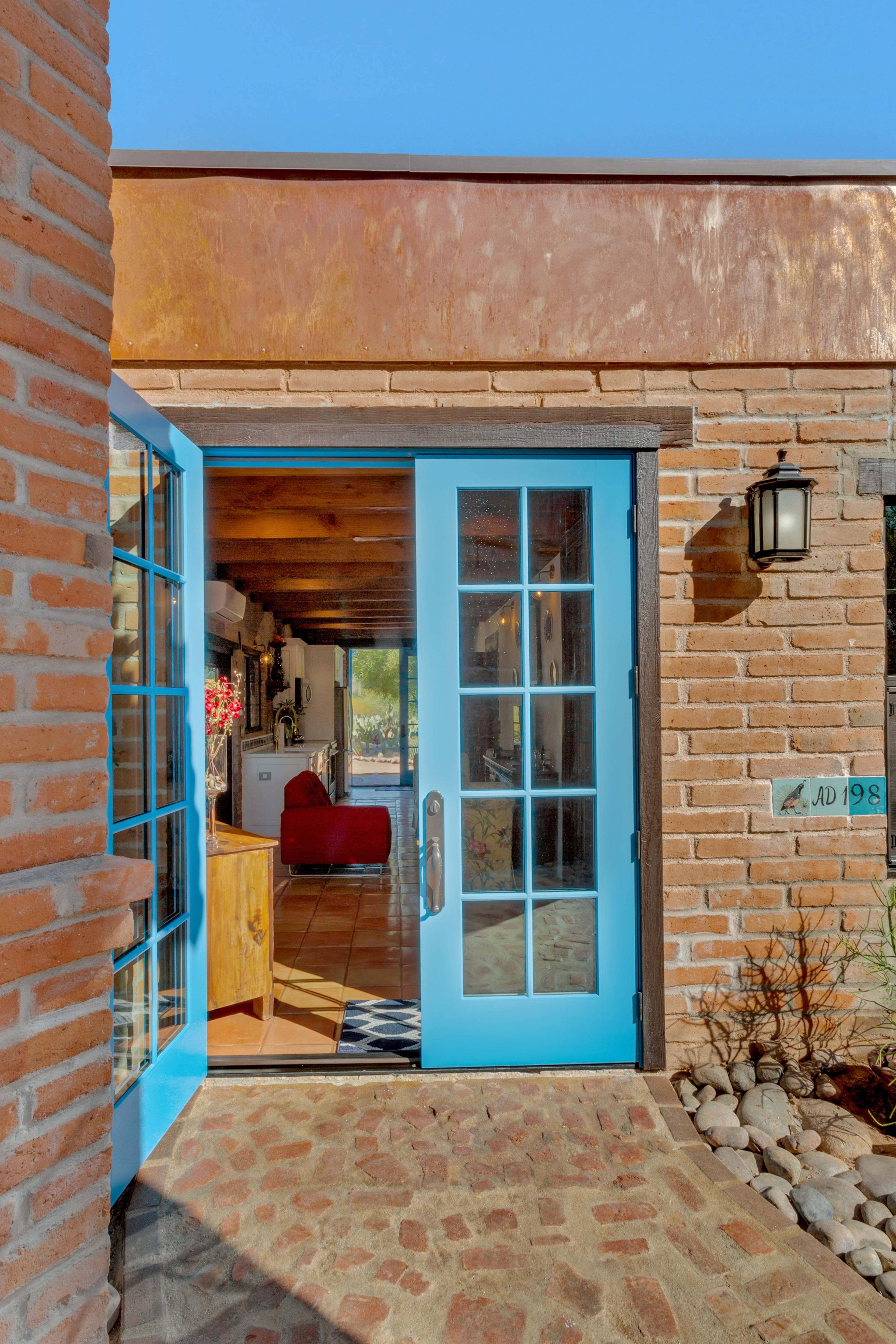 A bright blue door opening into a brick wall structure with a clear view of a cozy interior beyond.