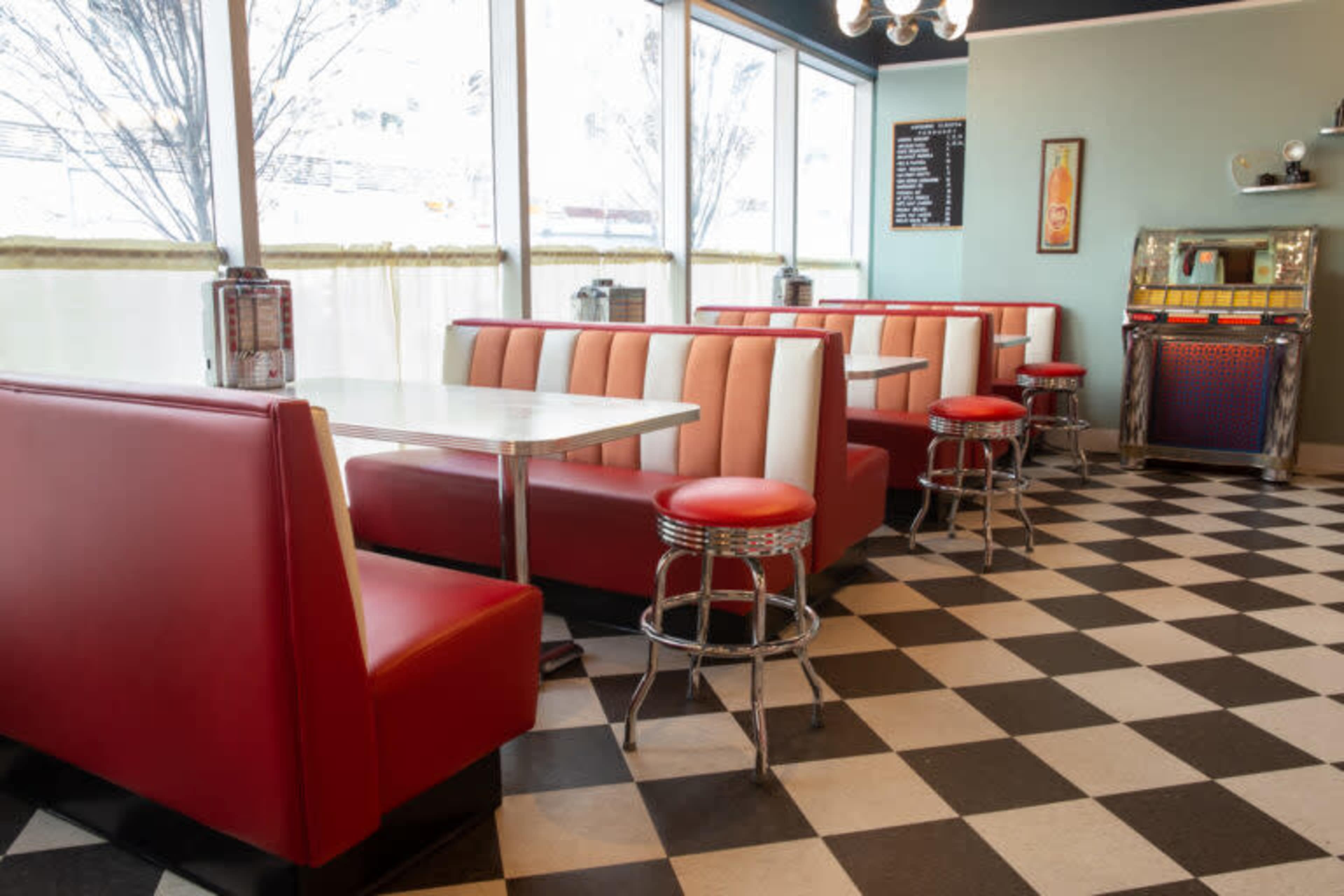 A retro-style diner with red and white vinyl booths, chrome stools, and a black and white checkered floor.