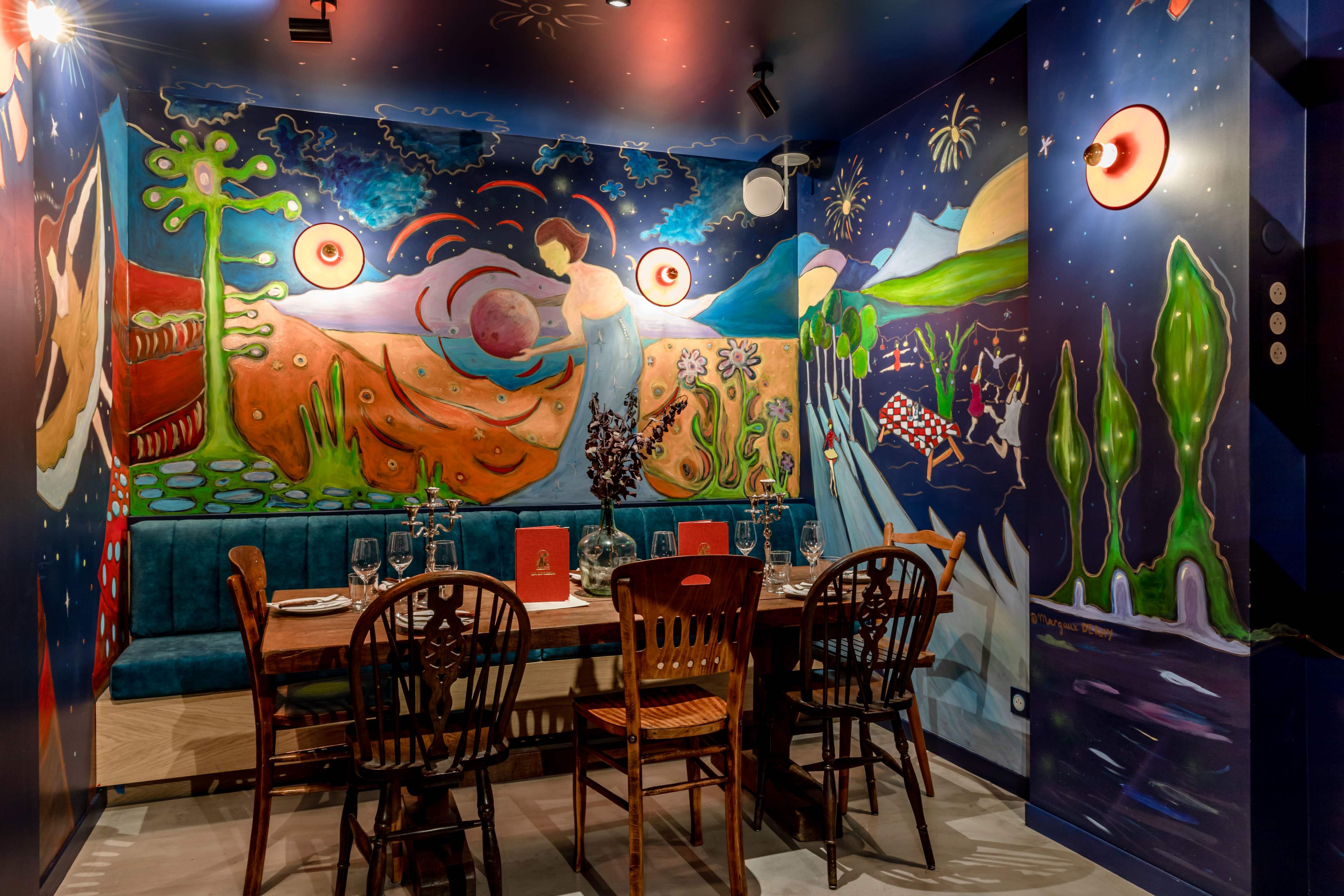 A vibrant dining area with a large, colorful mural on the walls, featuring a variety of abstract shapes and designs, and a wooden table set for a meal.