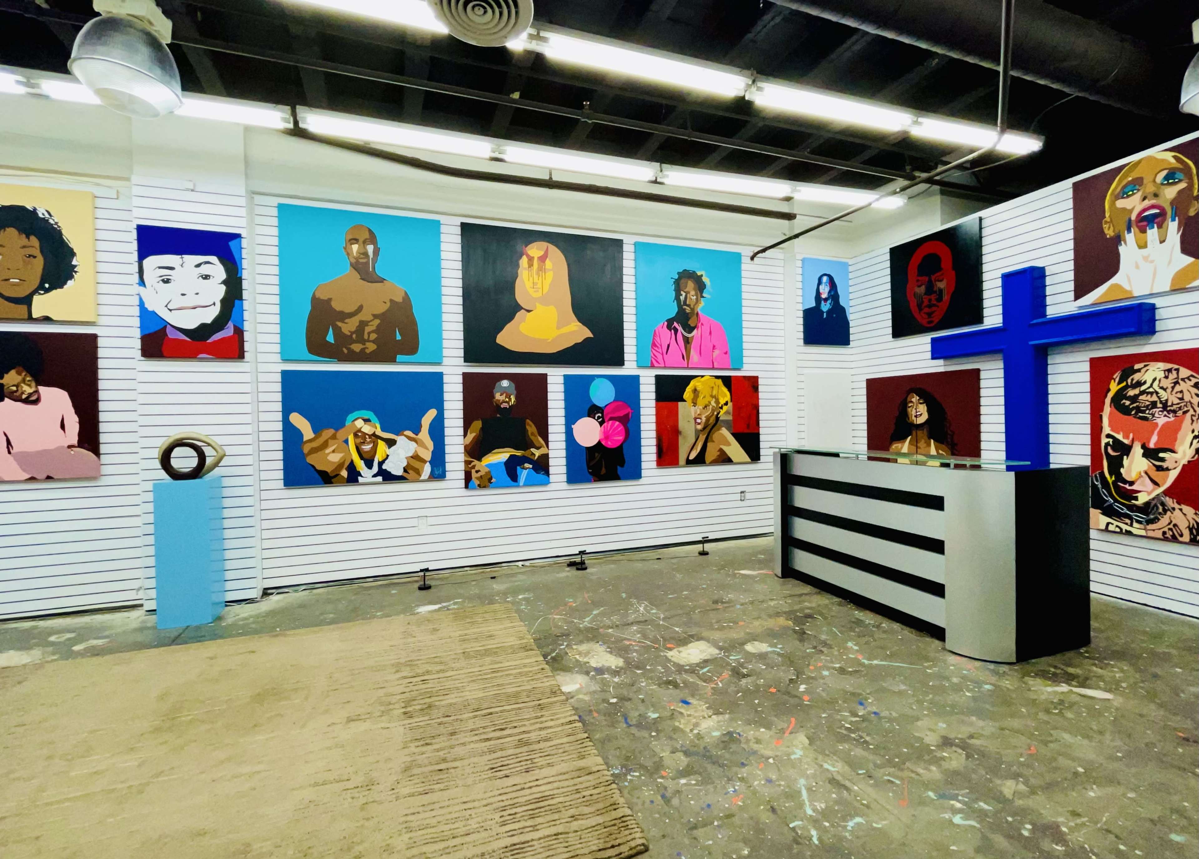 The image shows an art gallery interior featuring a series of colorful portraits on the walls and a modern reception desk in the foreground.
