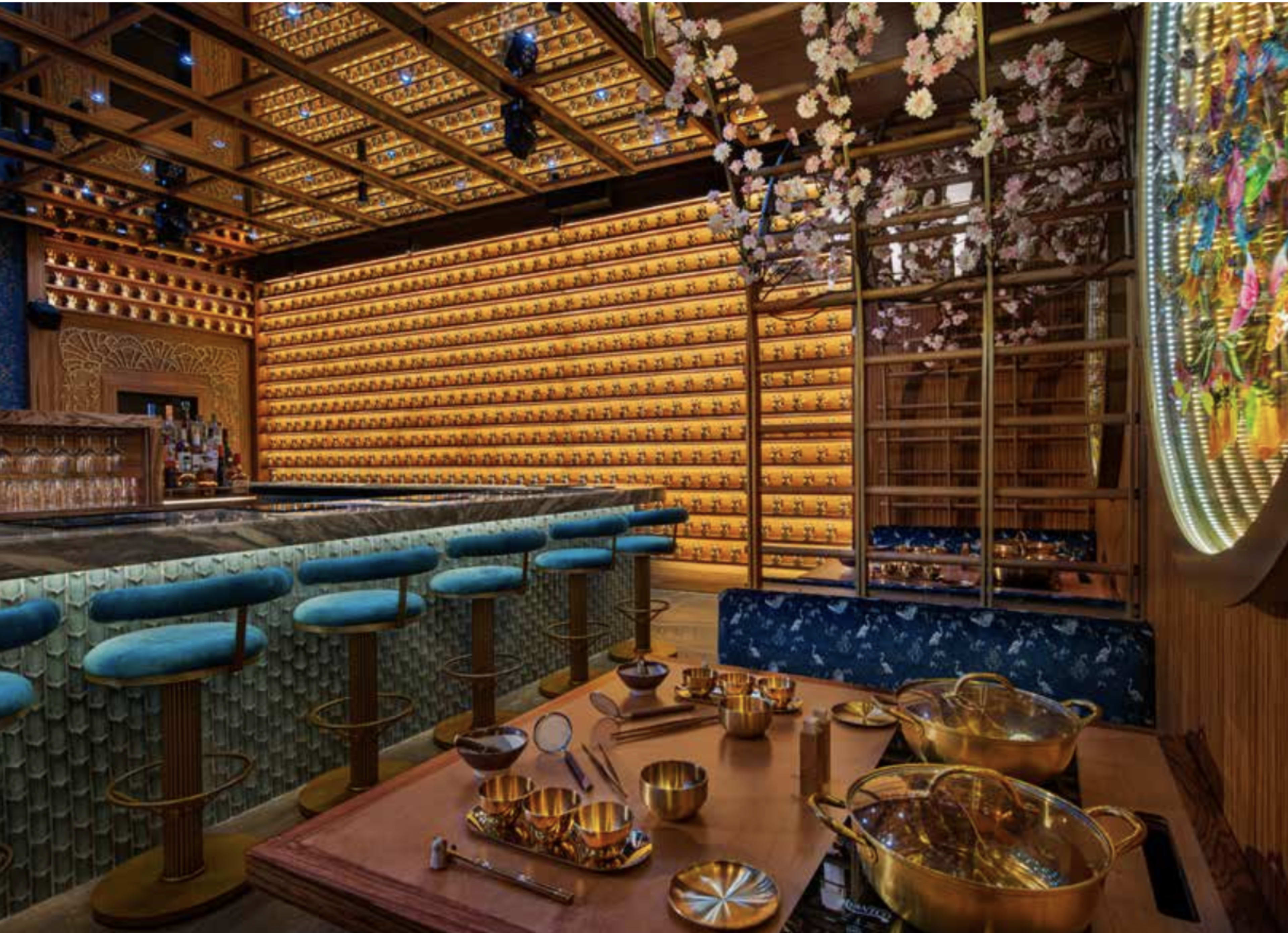 The image shows an upscale bar interior with a colorful backlit shelf, ornate decorations, and a seating area featuring blue bar stools.