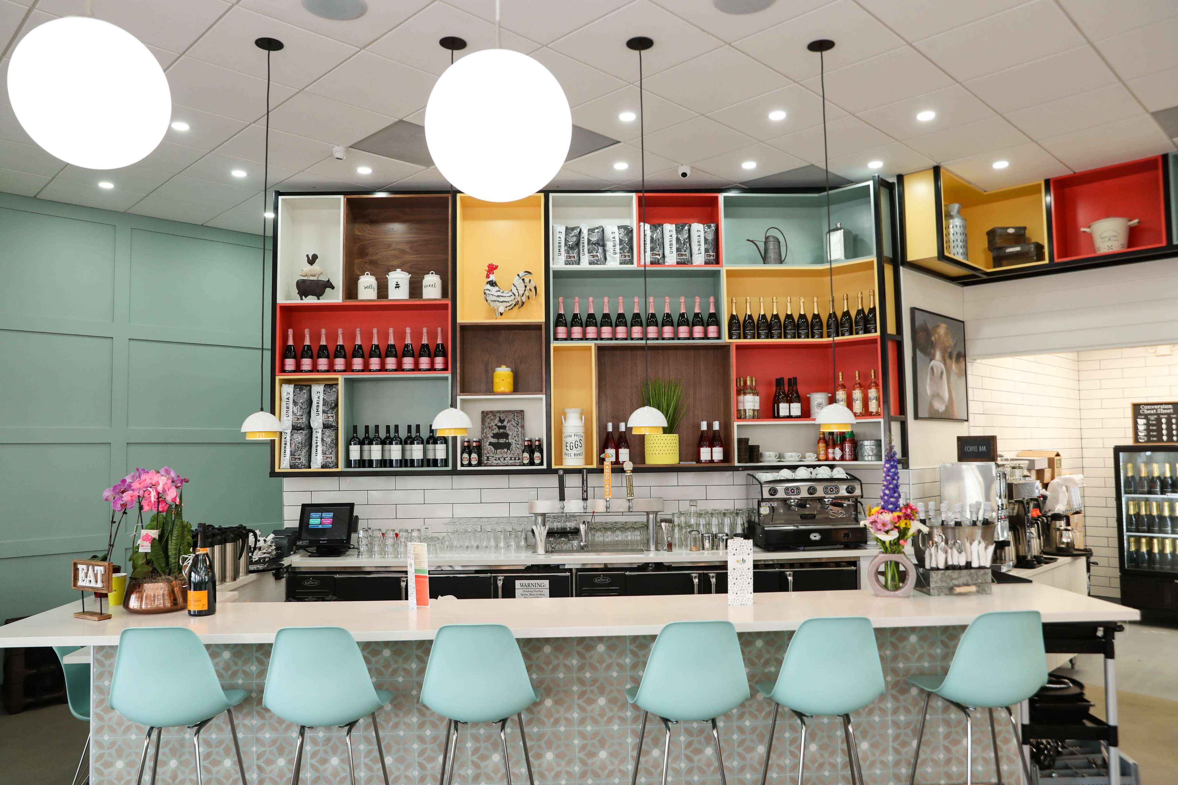 A modern café bar with colorful shelving displaying bottles and decorative items behind a counter with seating.
