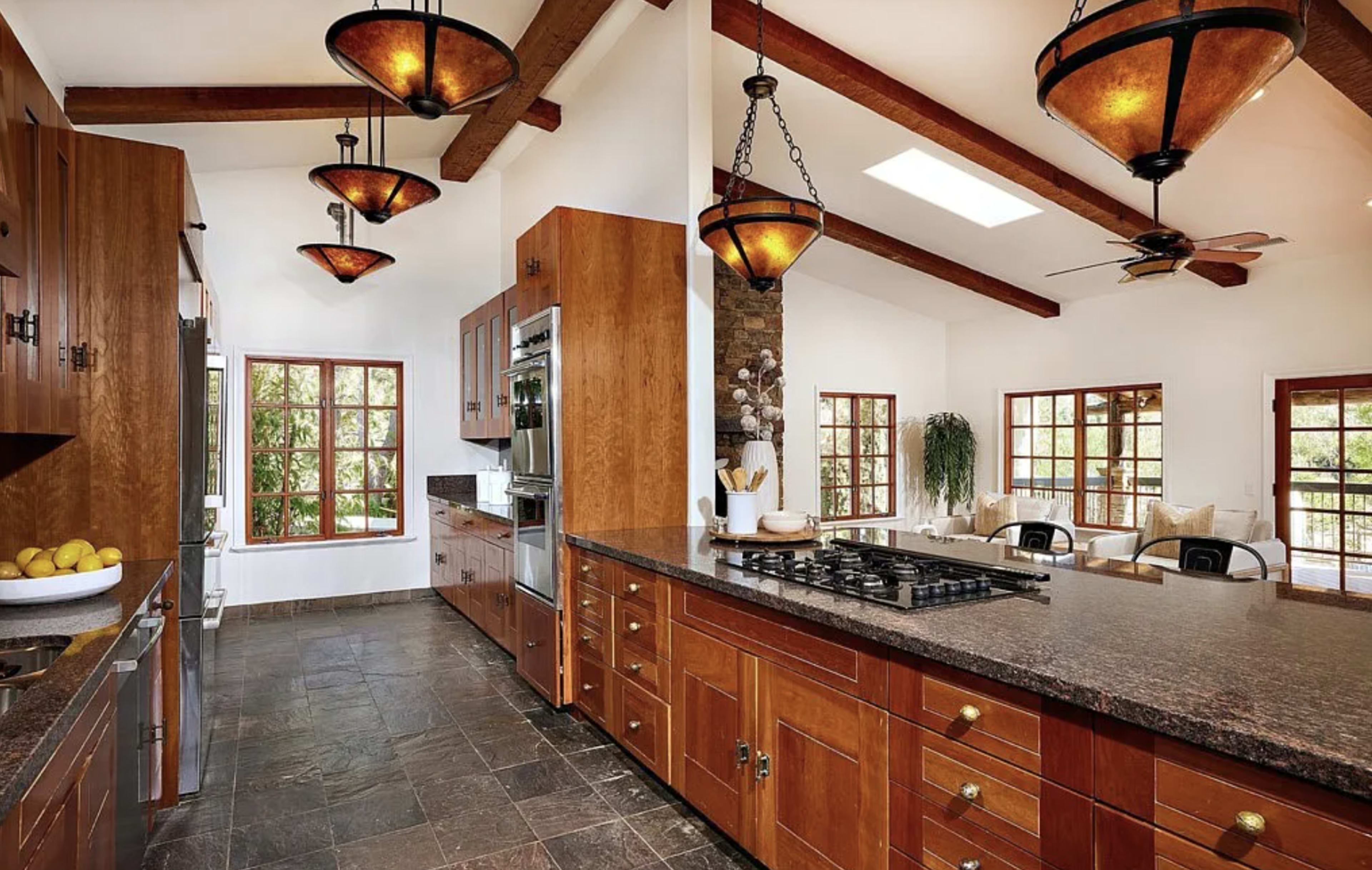 A spacious kitchen features dark countertops, wooden cabinetry, and large windows allowing natural light to fill the room.