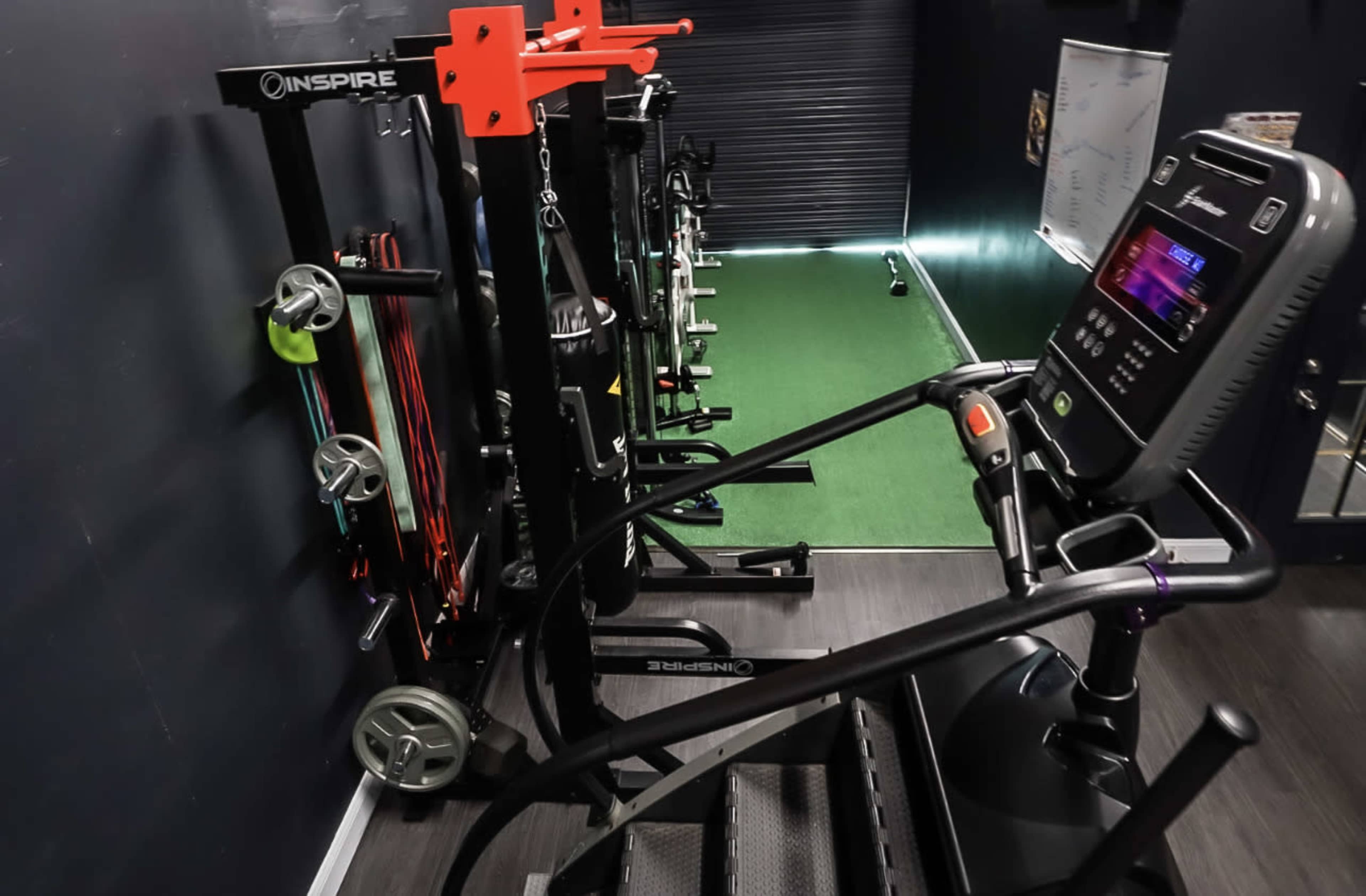 A gym interior with exercise equipment, including a stair climber and various resistance bands neatly organized on racks against a dark wall.
