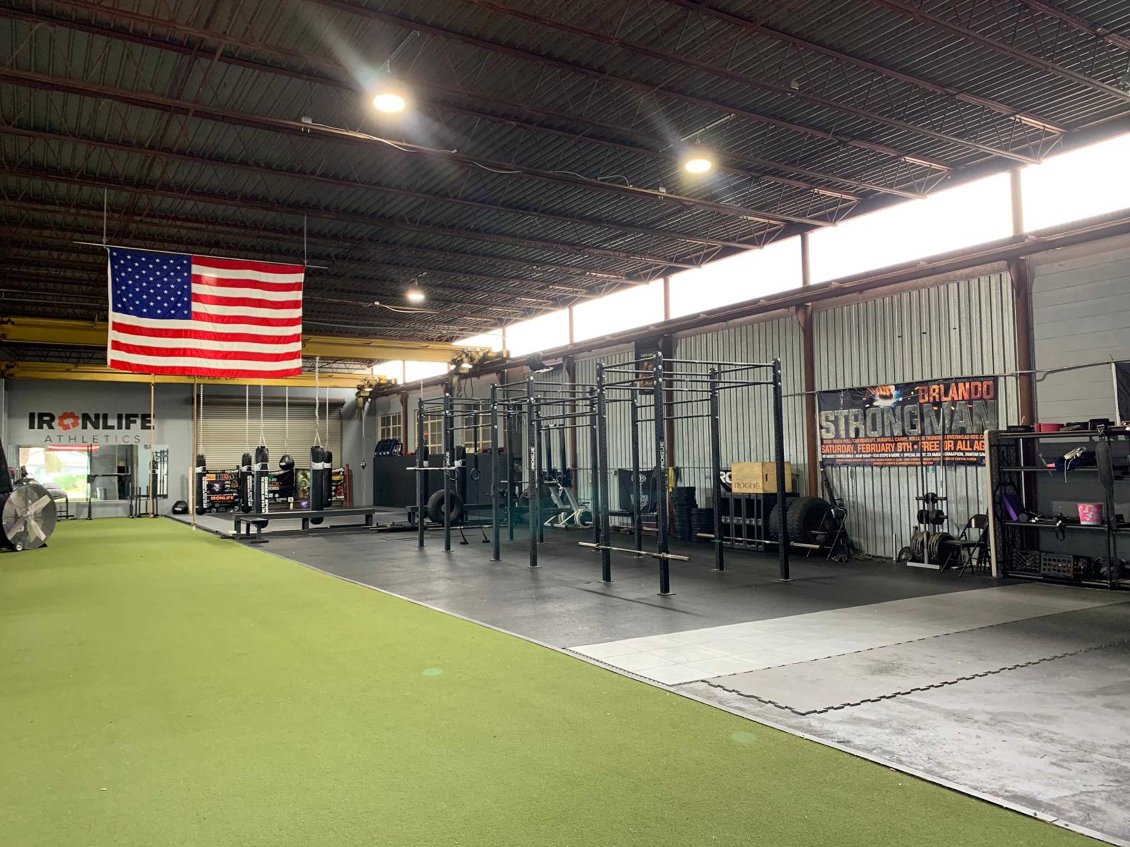 A fitness facility with gym equipment, a large American flag hanging from the ceiling, and turf flooring.