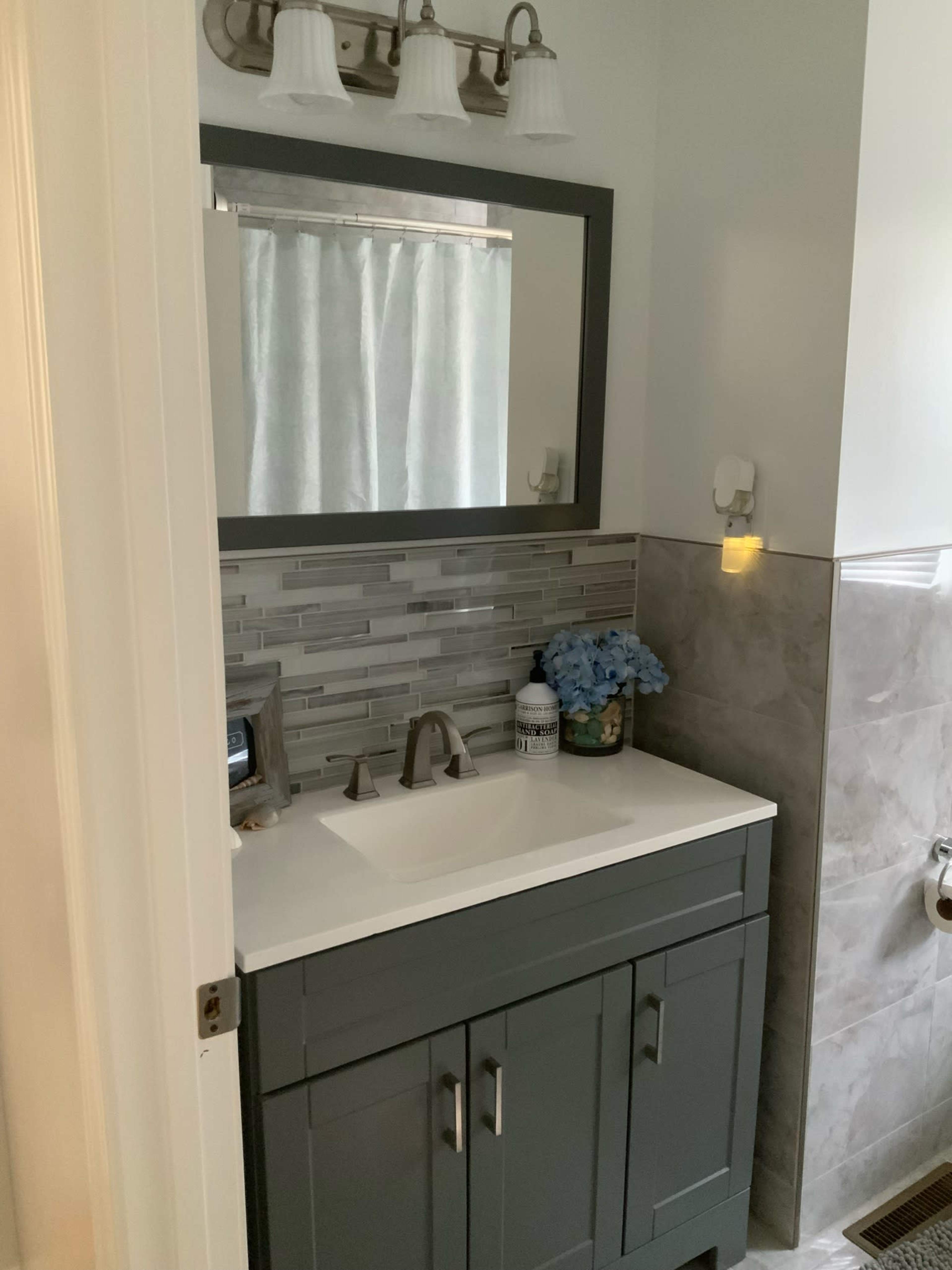 A modern bathroom vanity with a sink, gray cabinets, a decorative mirror, and blue hydrangea flowers.