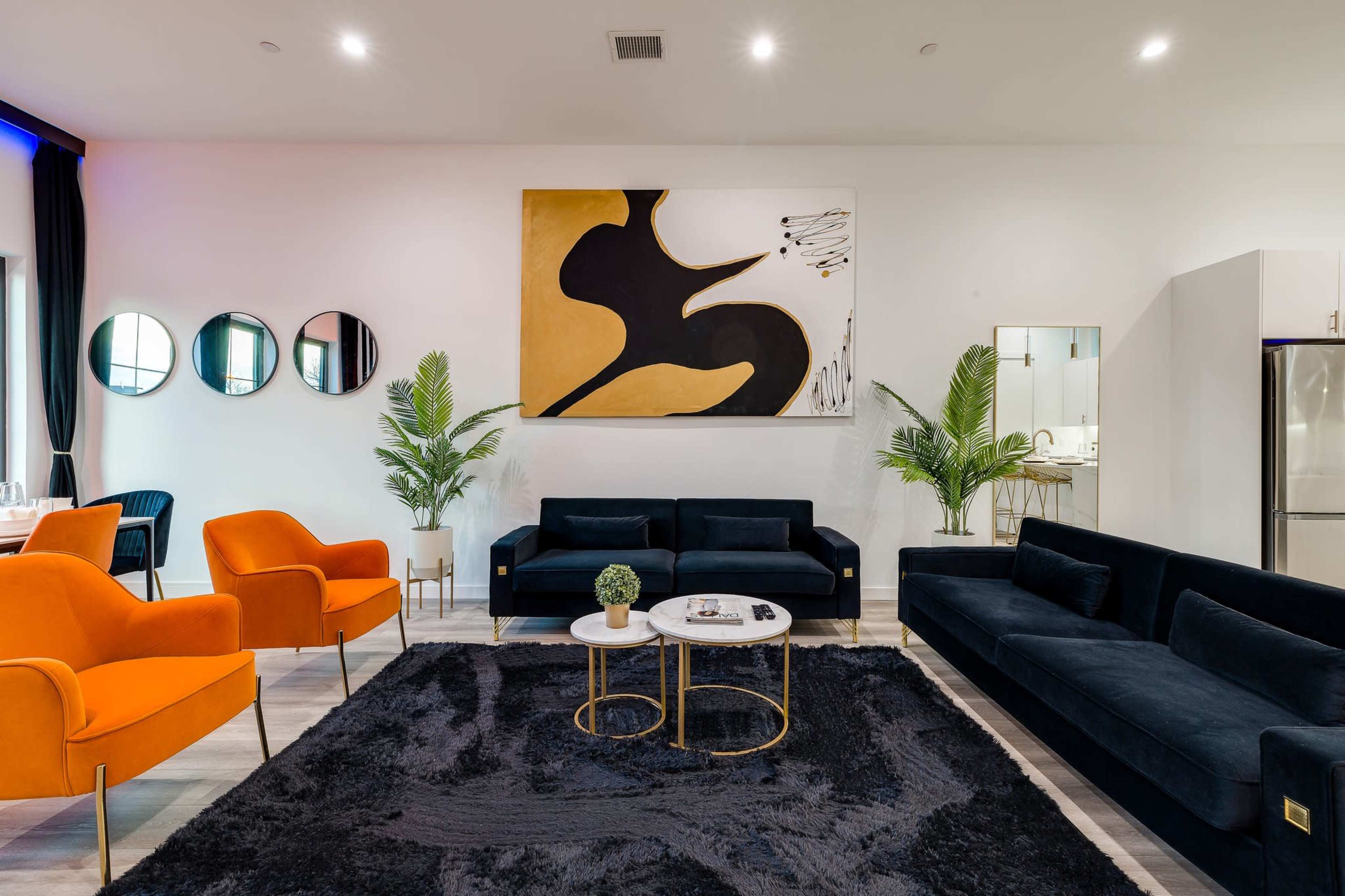 A modern living room with black and orange furniture, a large abstract painting, and round mirrors on the wall.