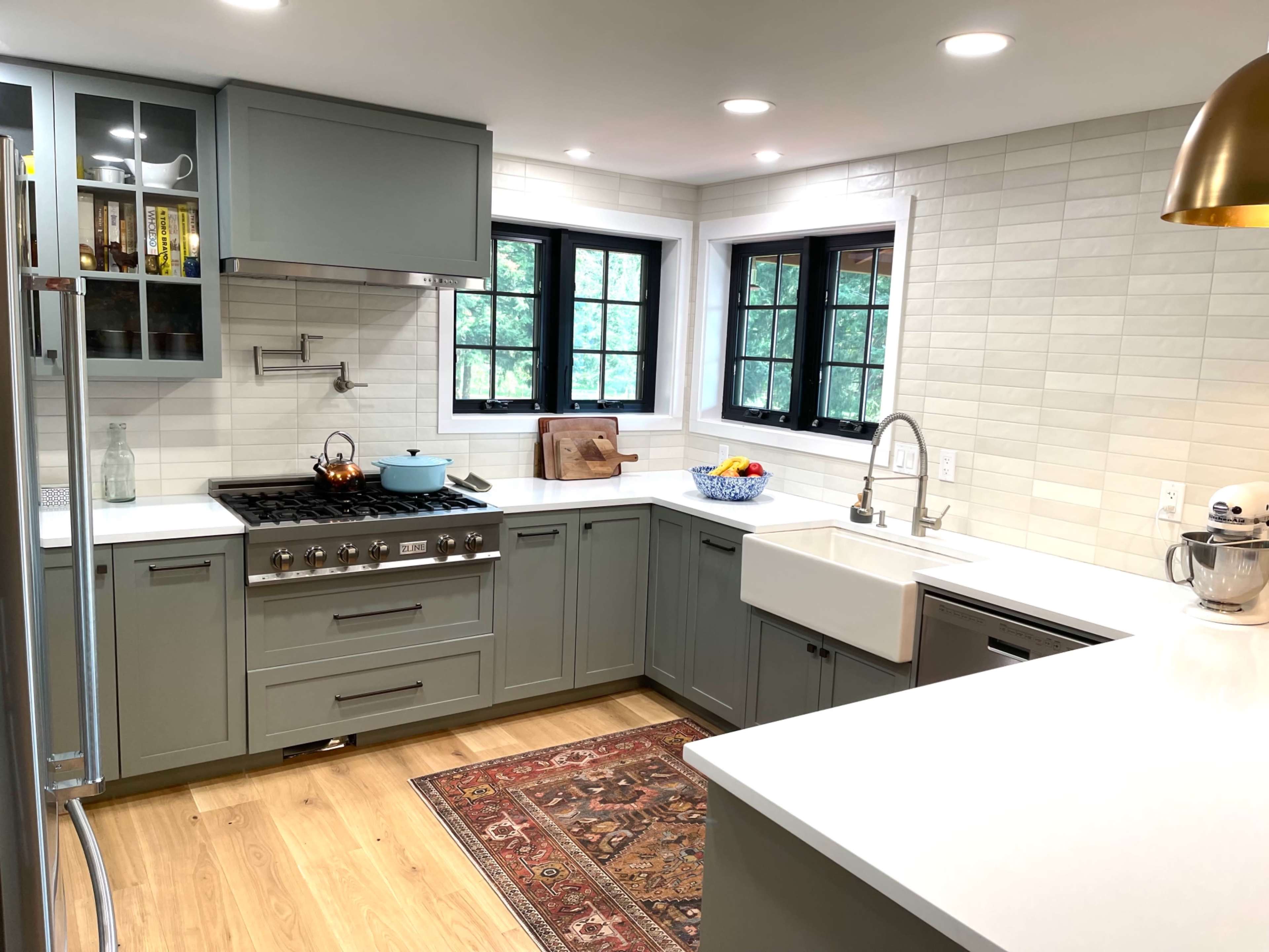 The kitchen features light green cabinetry, a farmhouse sink, stainless steel appliances, and a central island with a white countertop.