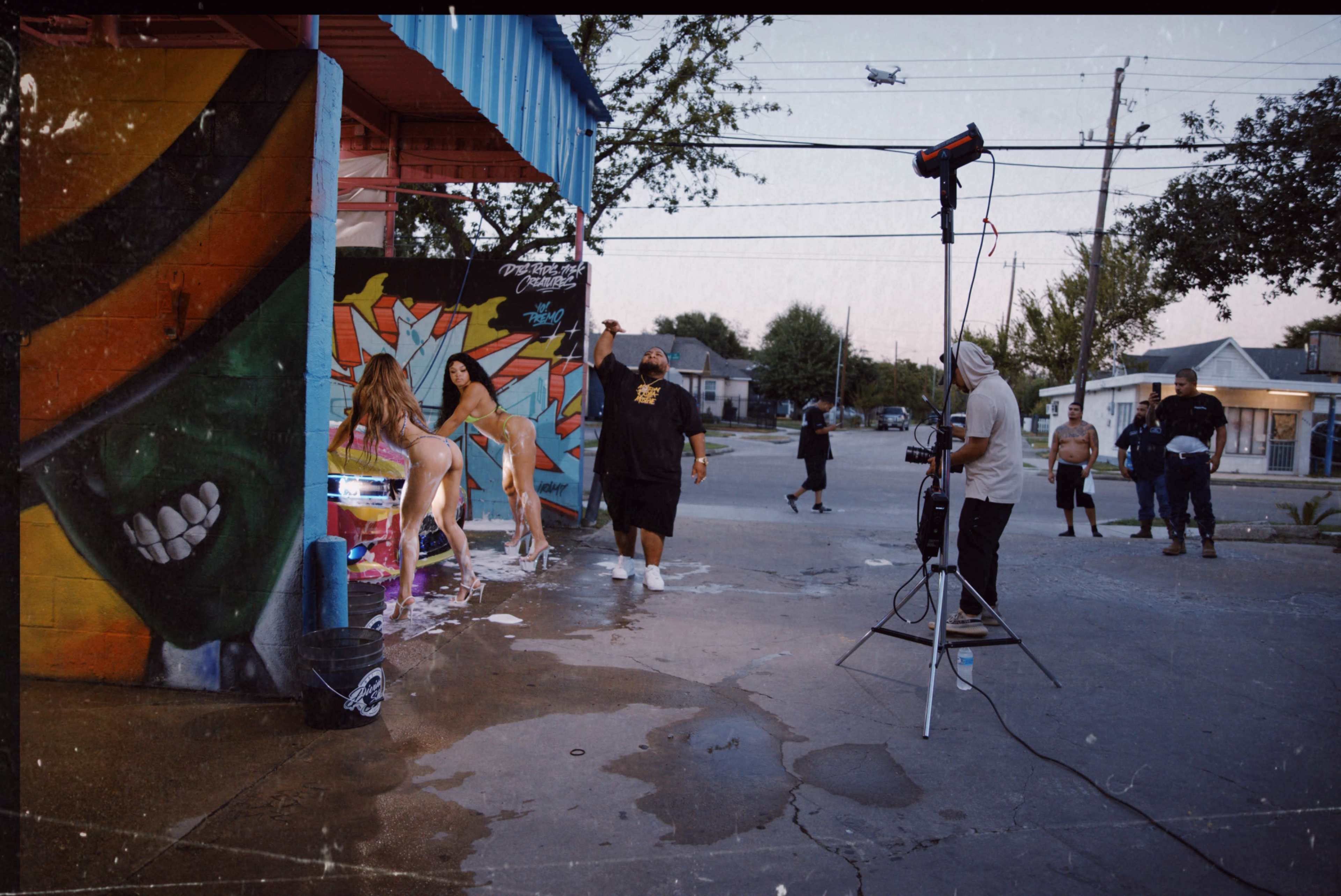 A group of people are engaged in a photoshoot outside a colorful mural, with one person posing in water while others prepare equipment and watch.