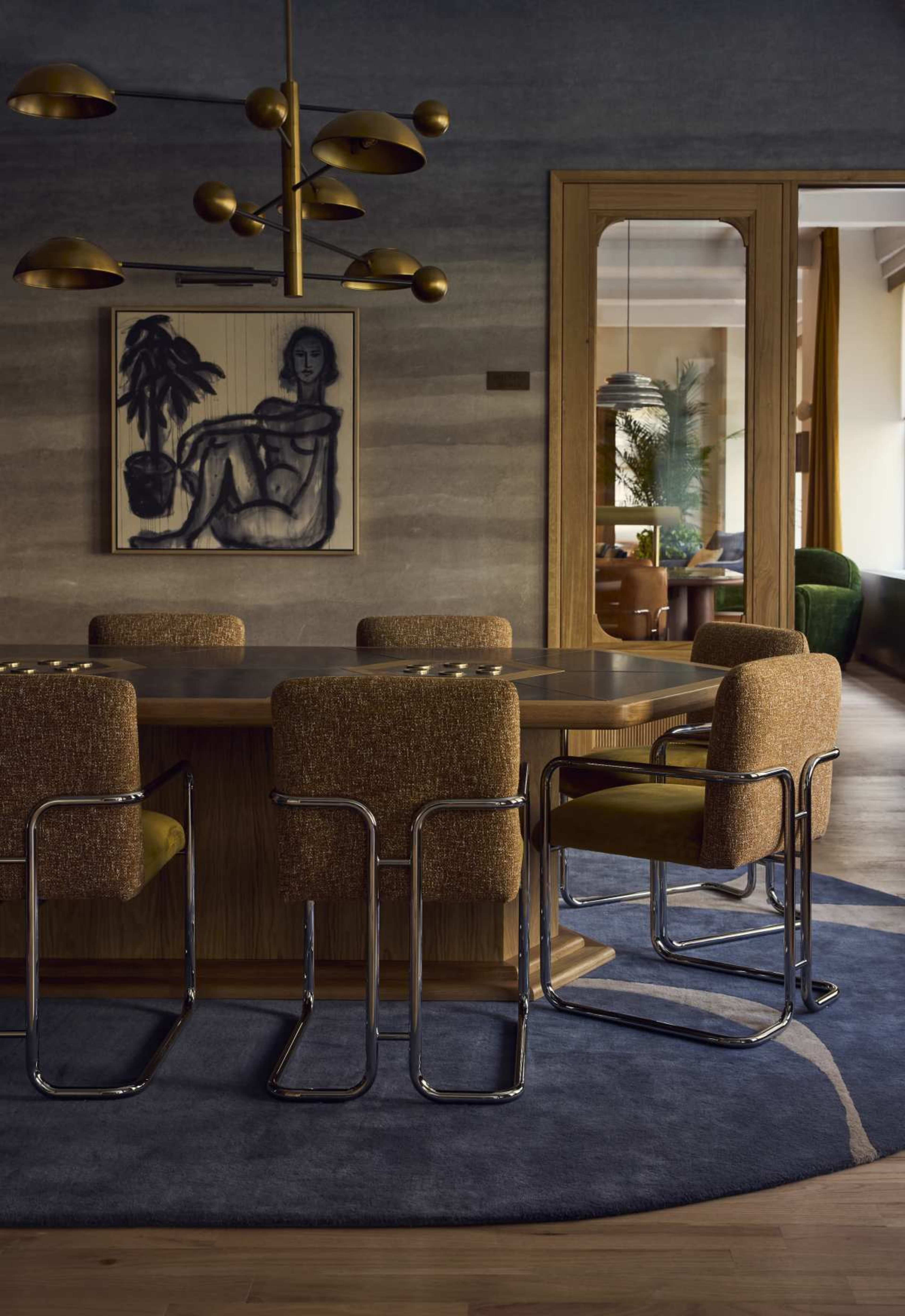 The image showcases a modern dining room featuring a circular wooden table surrounded by four upholstered chairs, with a large artwork on the wall and a pendant light above.