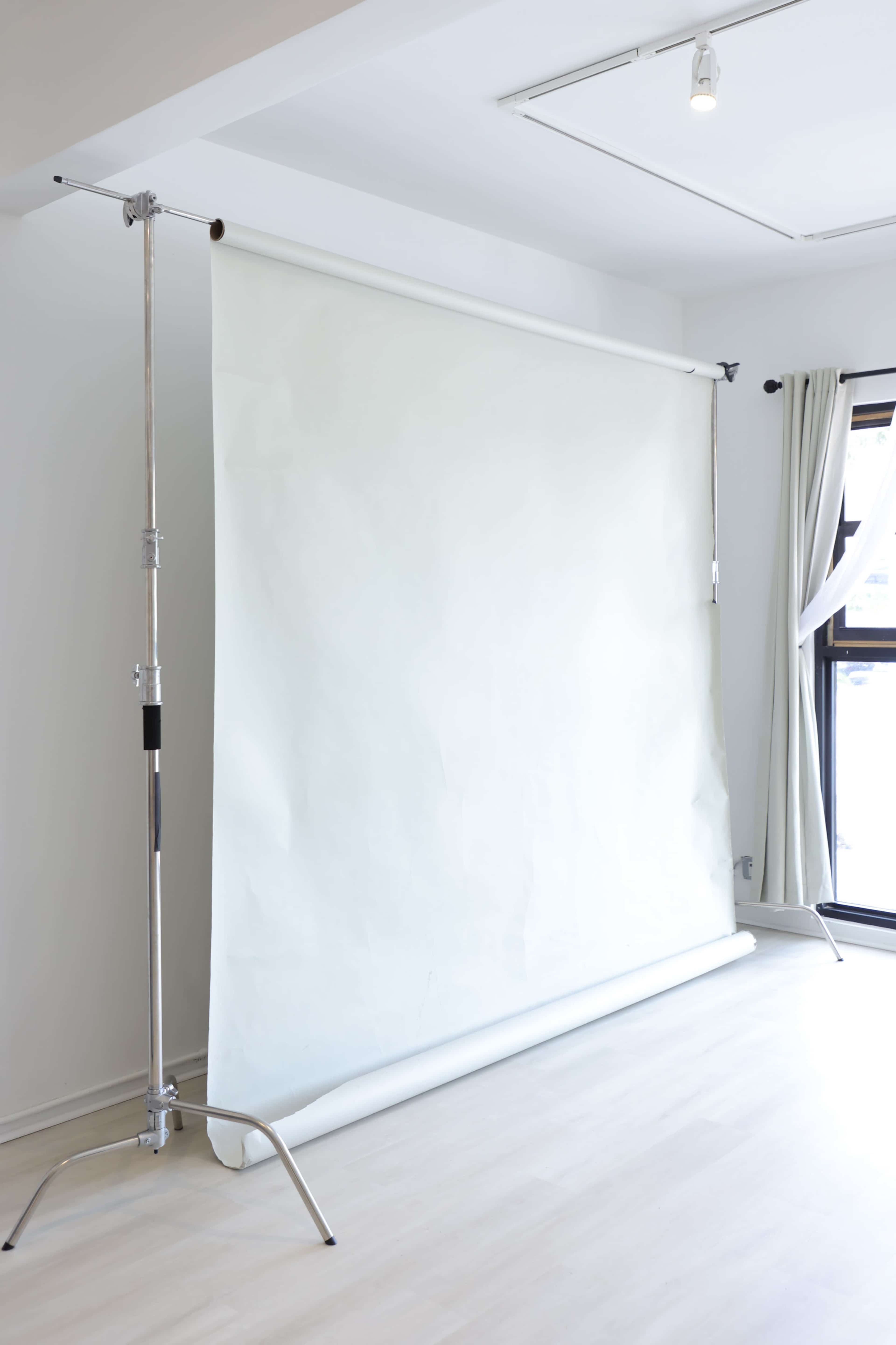 The image shows a white backdrop on a stand in a well-lit, minimalist room with wooden flooring and curtains.