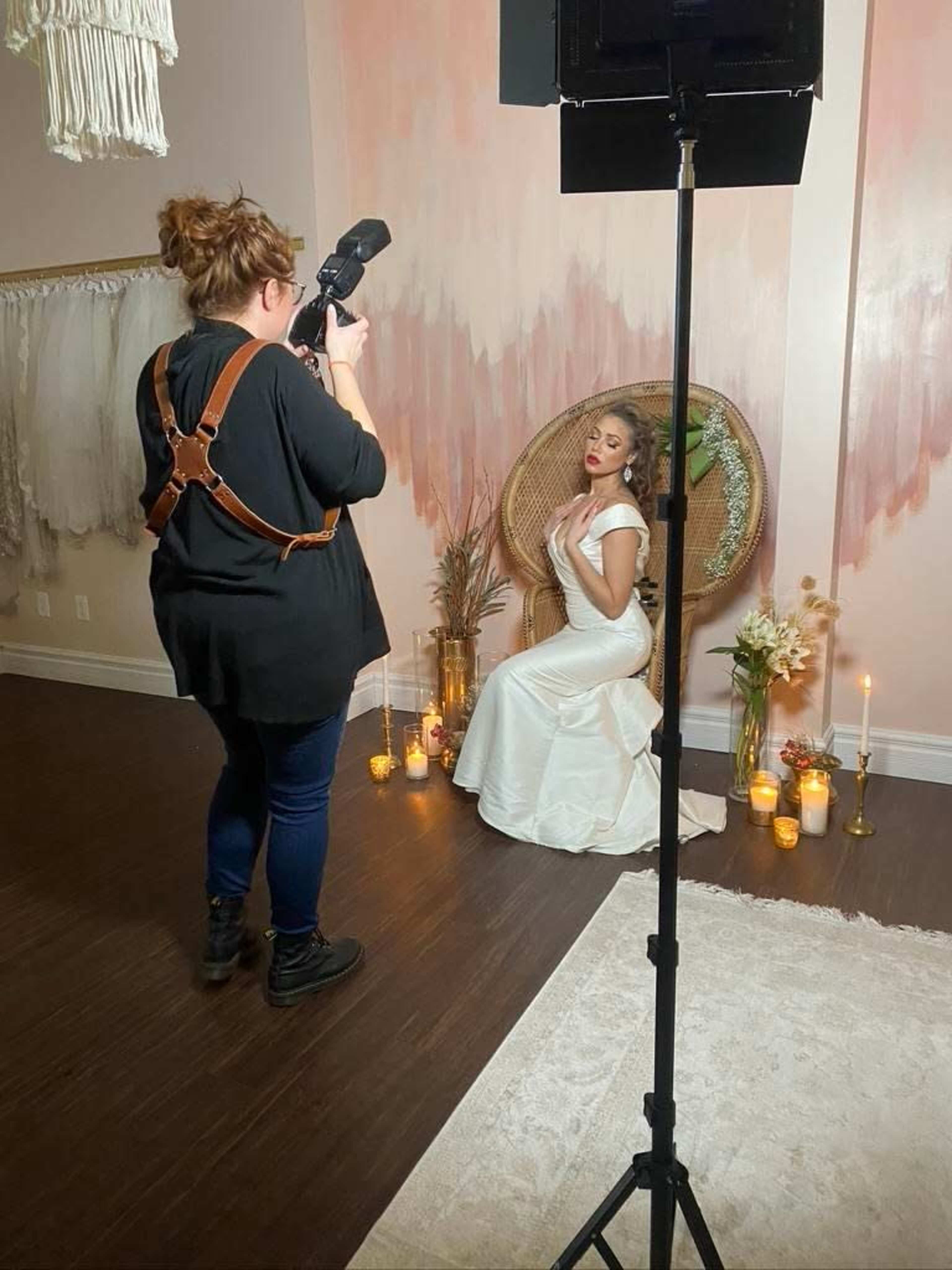 A photographer captures an image of a model in a white dress sitting in front of a decorative backdrop with candles and flowers.