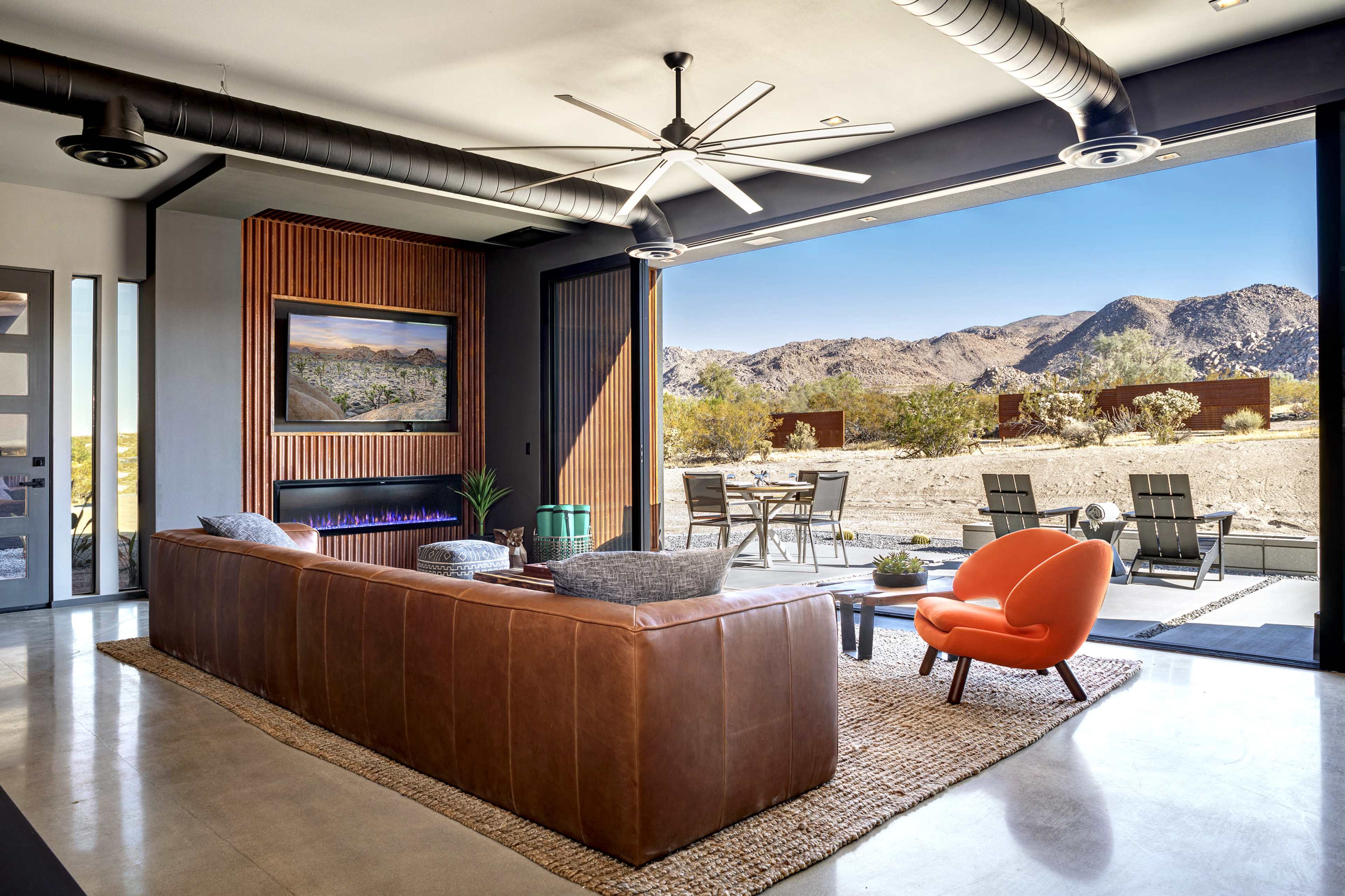 A modern living room with a leather sofa opens to a patio overlooking a desert landscape.