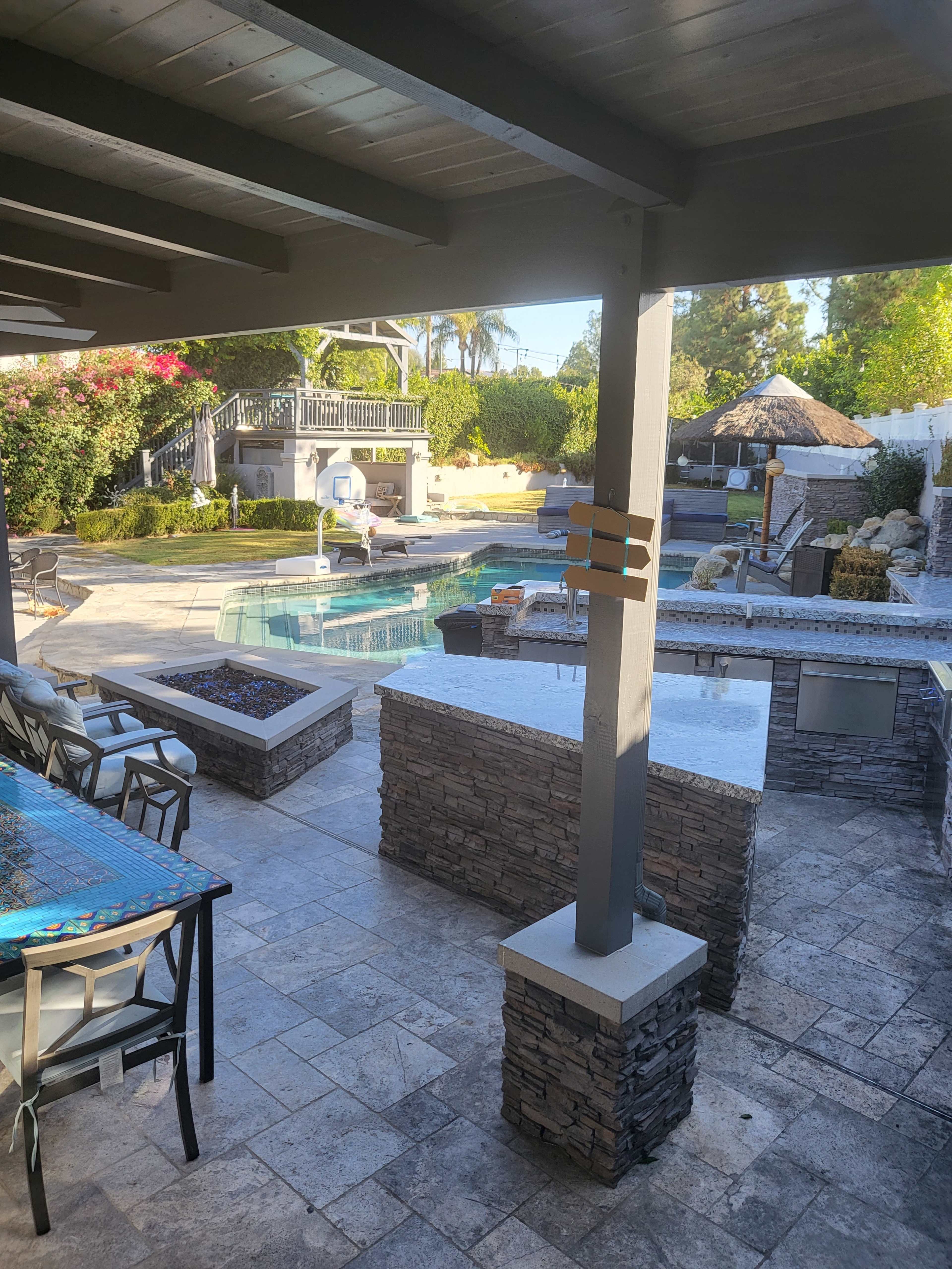 A well-designed backyard with a swimming pool, stone patio, and a bar area under a covered patio.