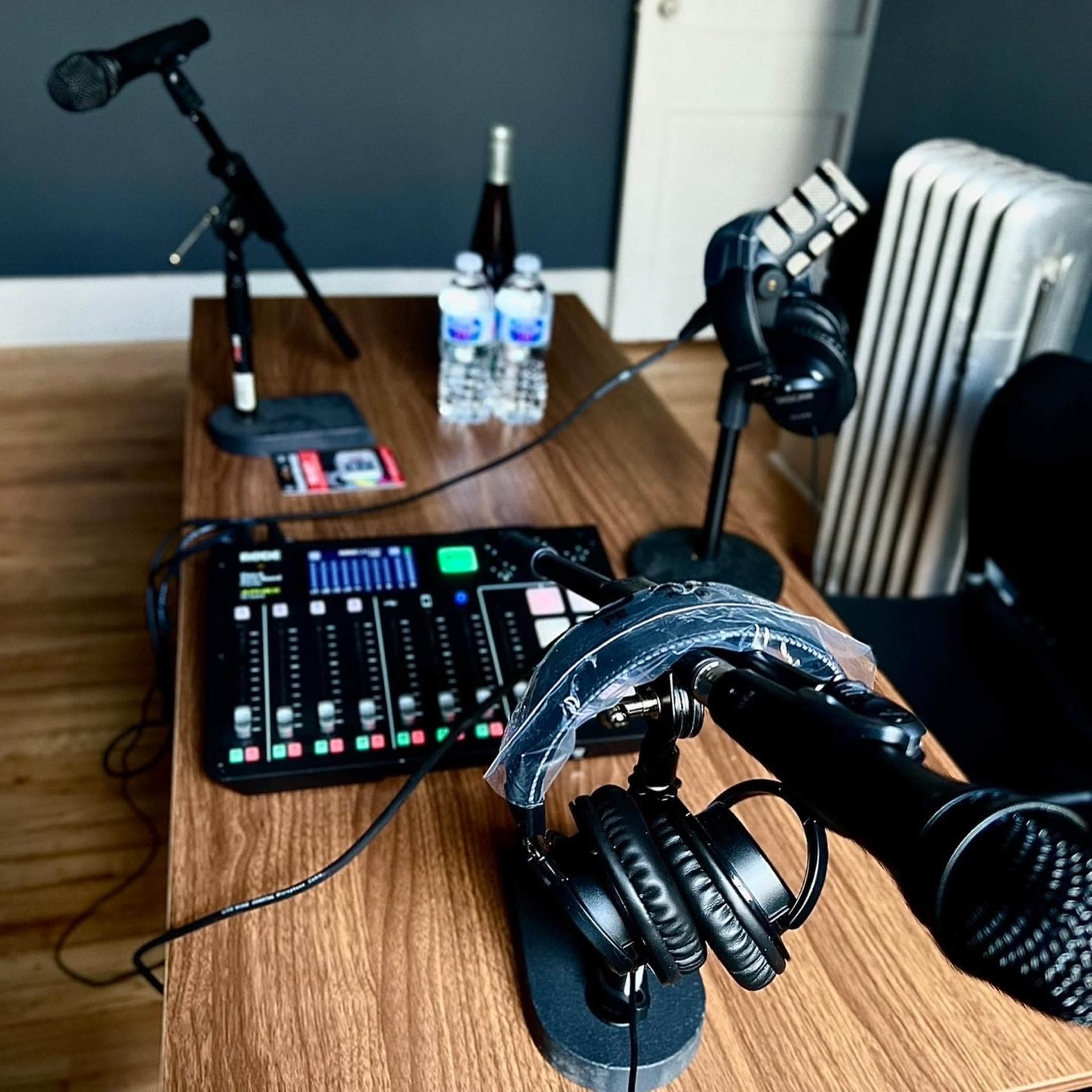 A wooden table equipped with microphones, headphones, a sound mixer, and bottled water in a sparsely furnished room.