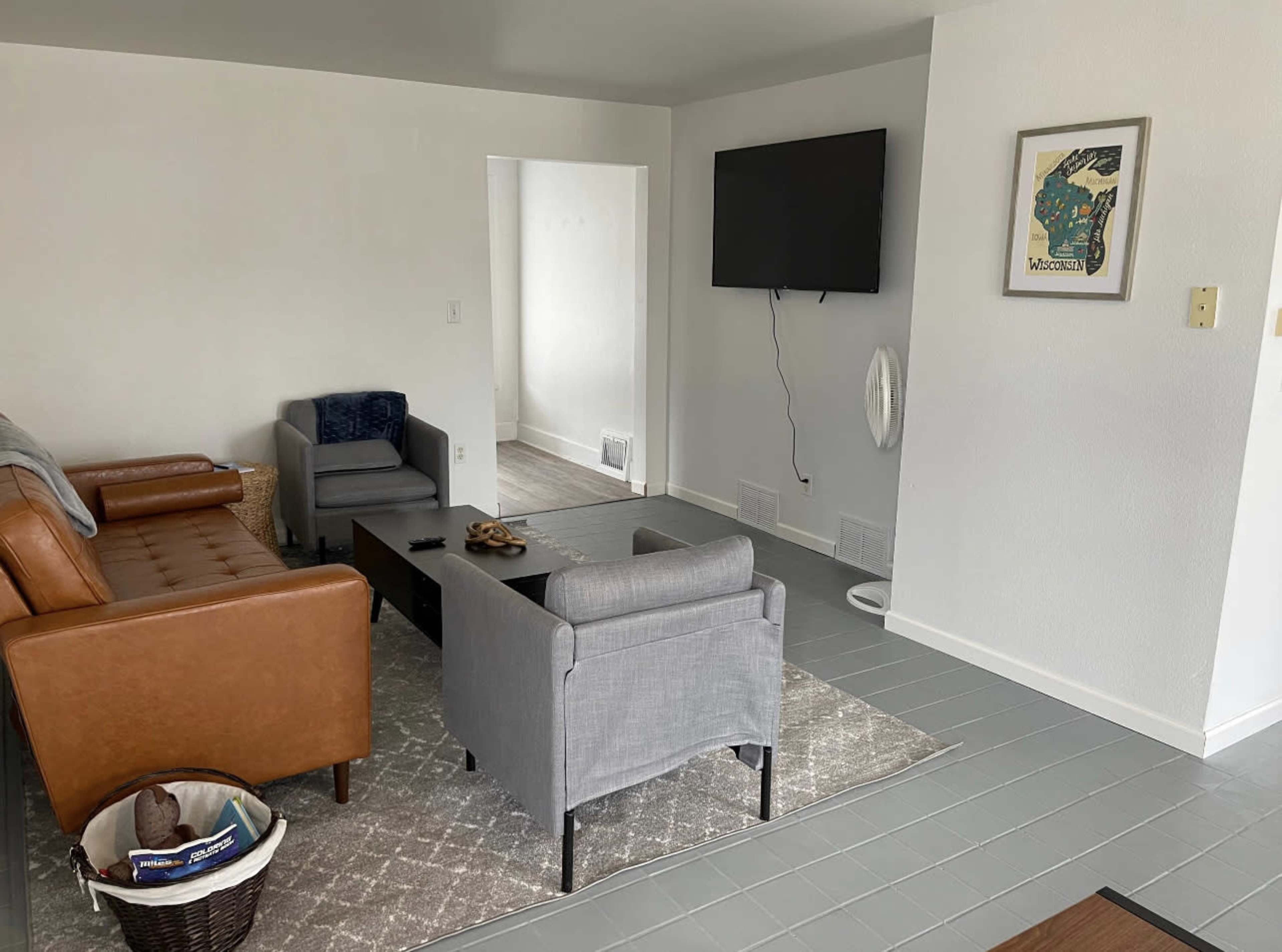 A modern living room with a brown leather sofa, two gray armchairs, a coffee table, and a wall-mounted television.