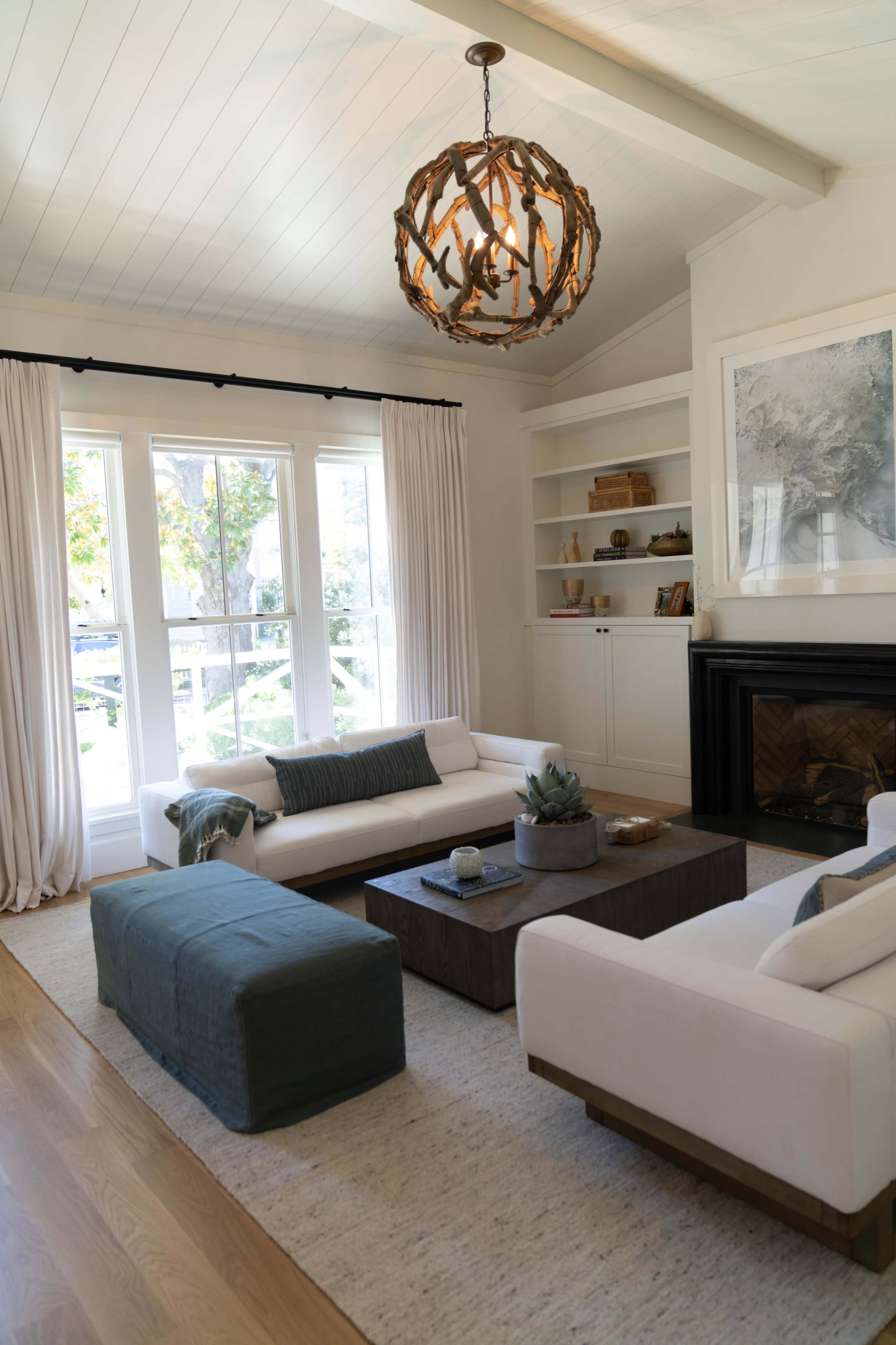 The living room features two white sofas, a dark wooden coffee table, and a decorative light fixture hanging from the ceiling, with large windows allowing natural light to enter.