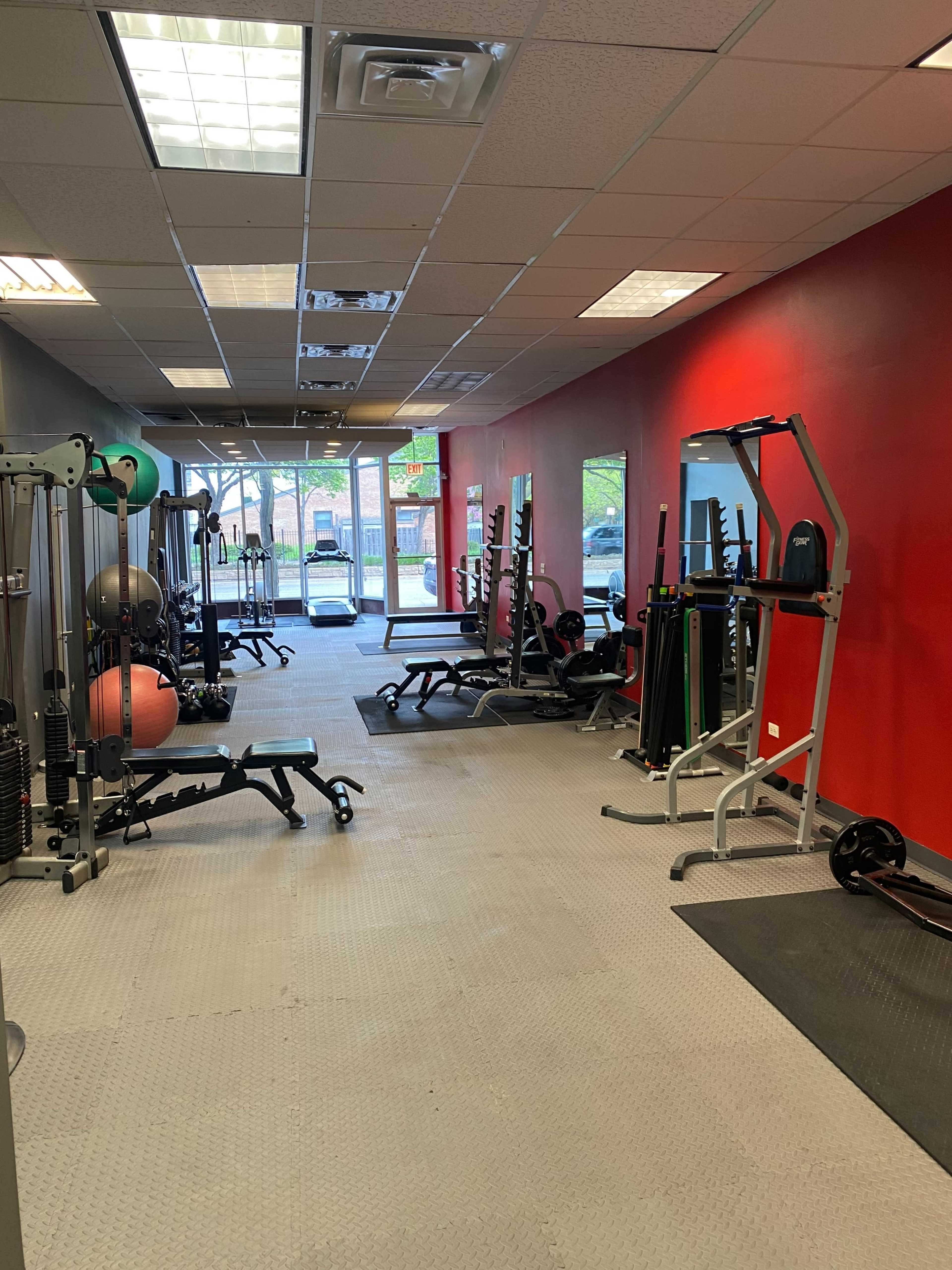 A spacious gym interior with various exercise equipment and large windows on one side.