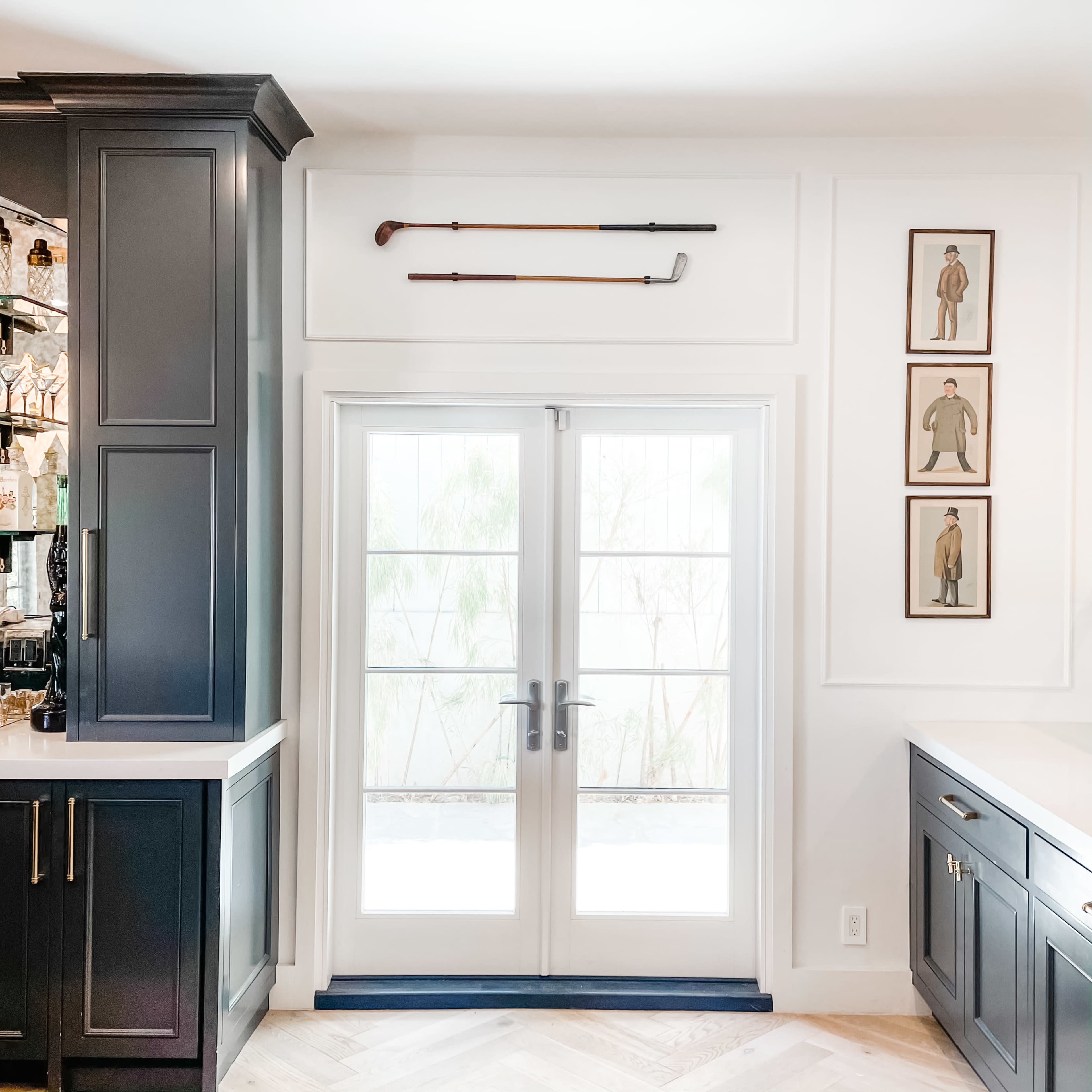 The image shows a modern kitchen corner featuring a pair of French doors, a wall with framed vintage golf attire, and golf clubs displayed above the doors.