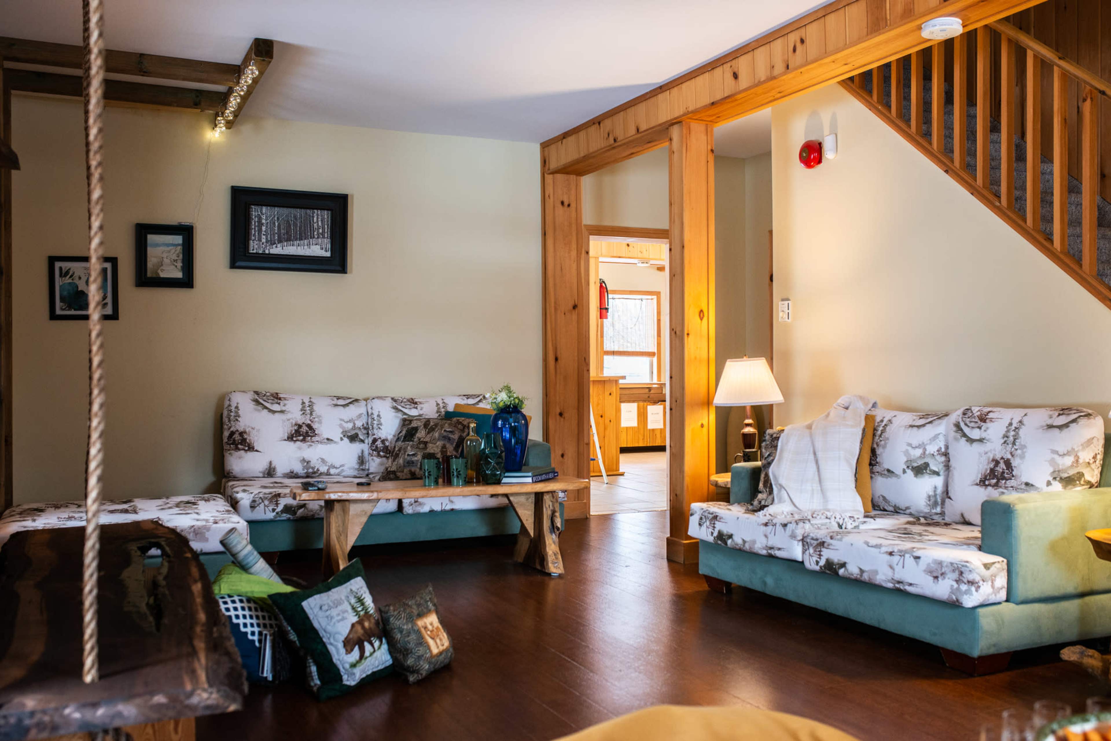 A cozy living room with two distinct sofas, a wooden coffee table, and a wooden staircase leading to another area.