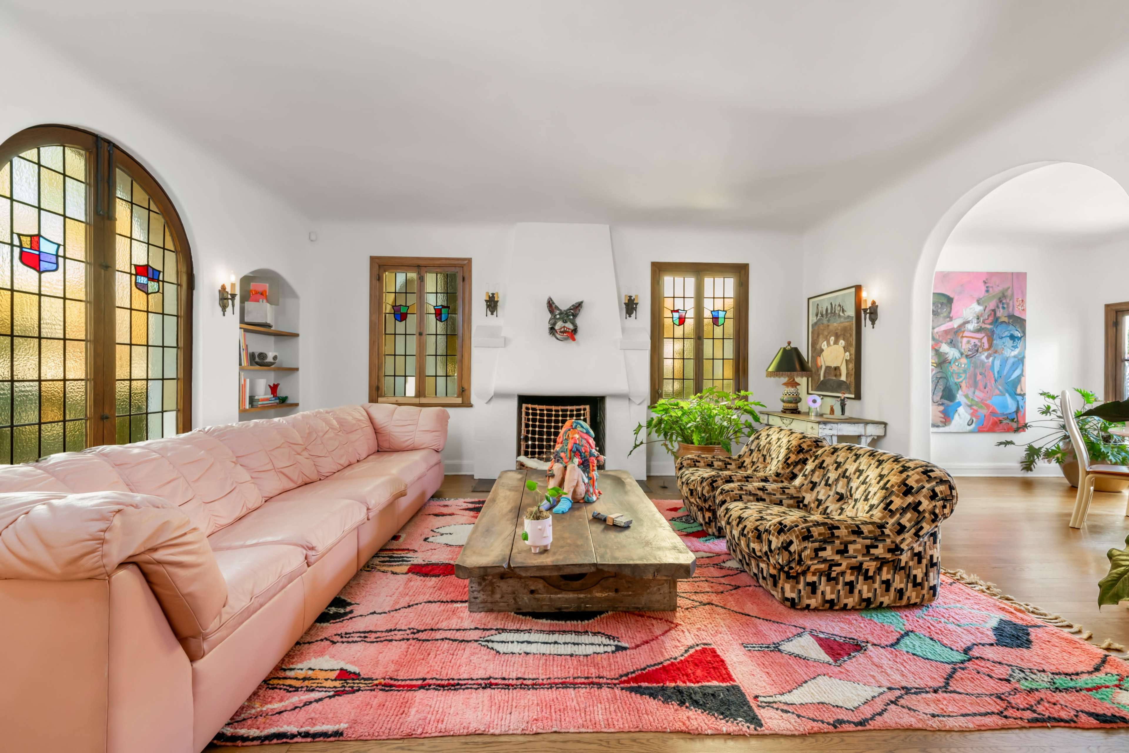 A spacious living room features a pink sofa, an animal-print chair, a wooden coffee table, and stained glass windows.