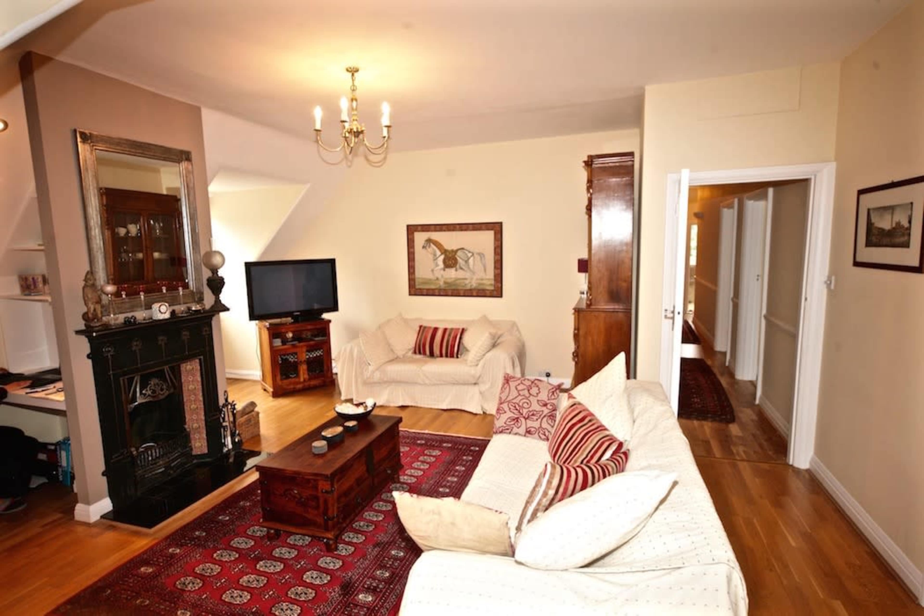 The living room features a fireplace, a television, two sofas, and a coffee table, with an adjoining hallway visible in the background.
