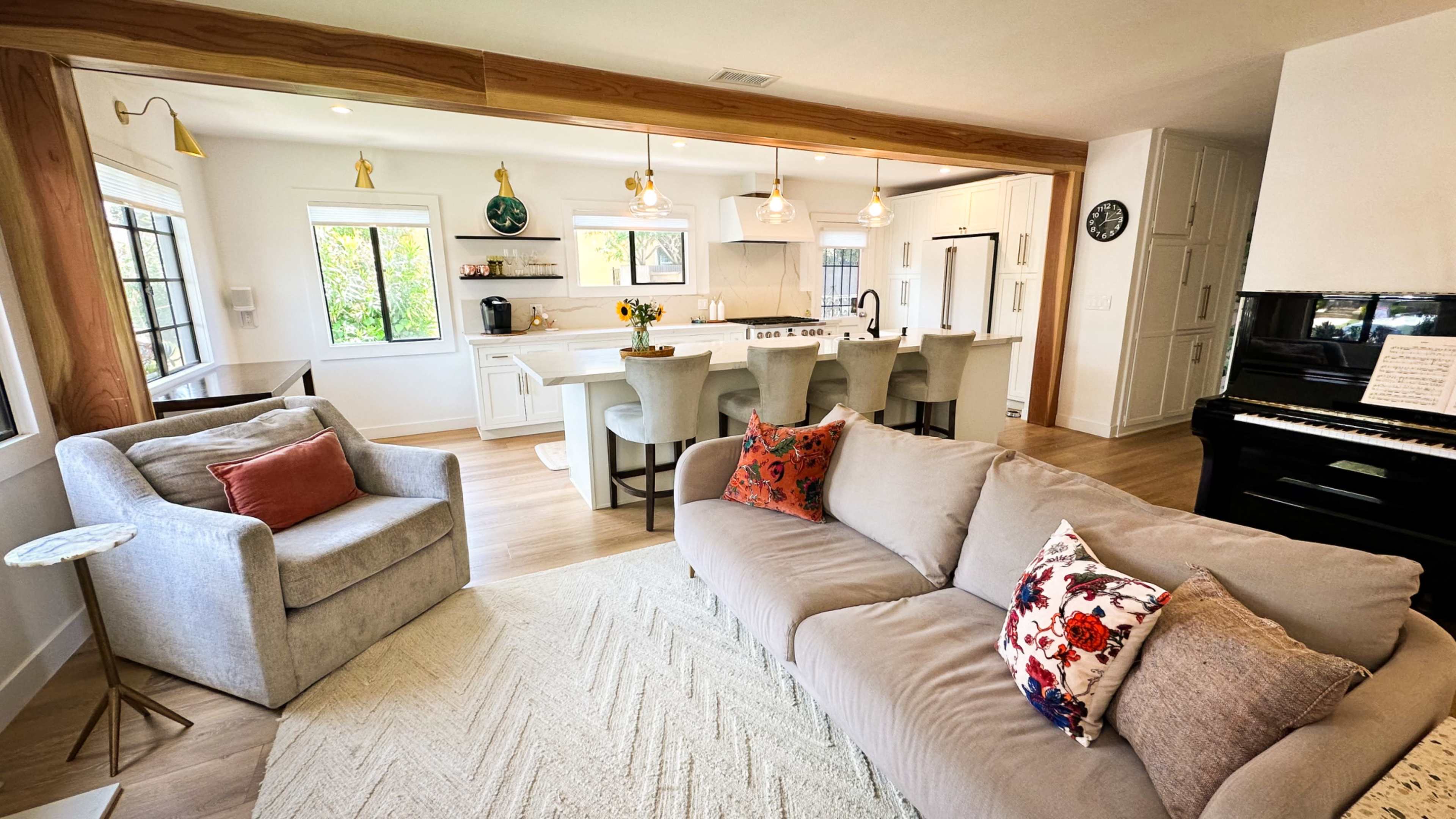 The image shows a modern living area with a gray couch, accent pillows, a small side table, and a kitchen in the background featuring a large island and white cabinetry.