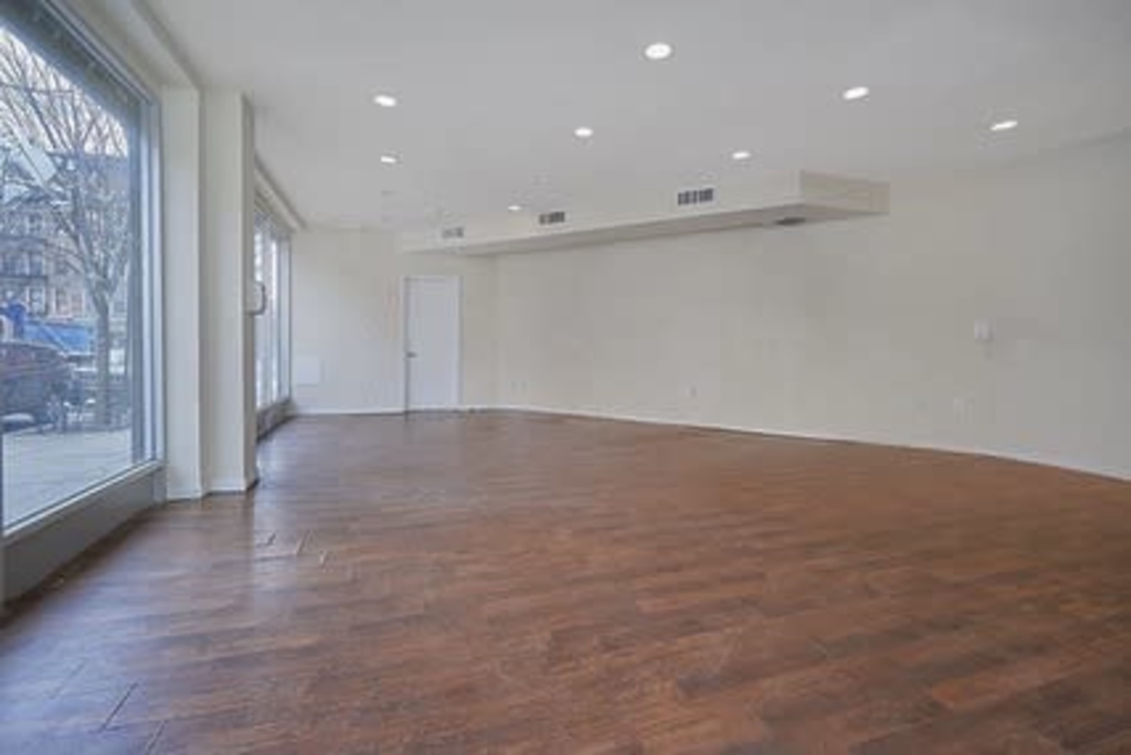 An empty room with wooden flooring, large windows, and white walls.
