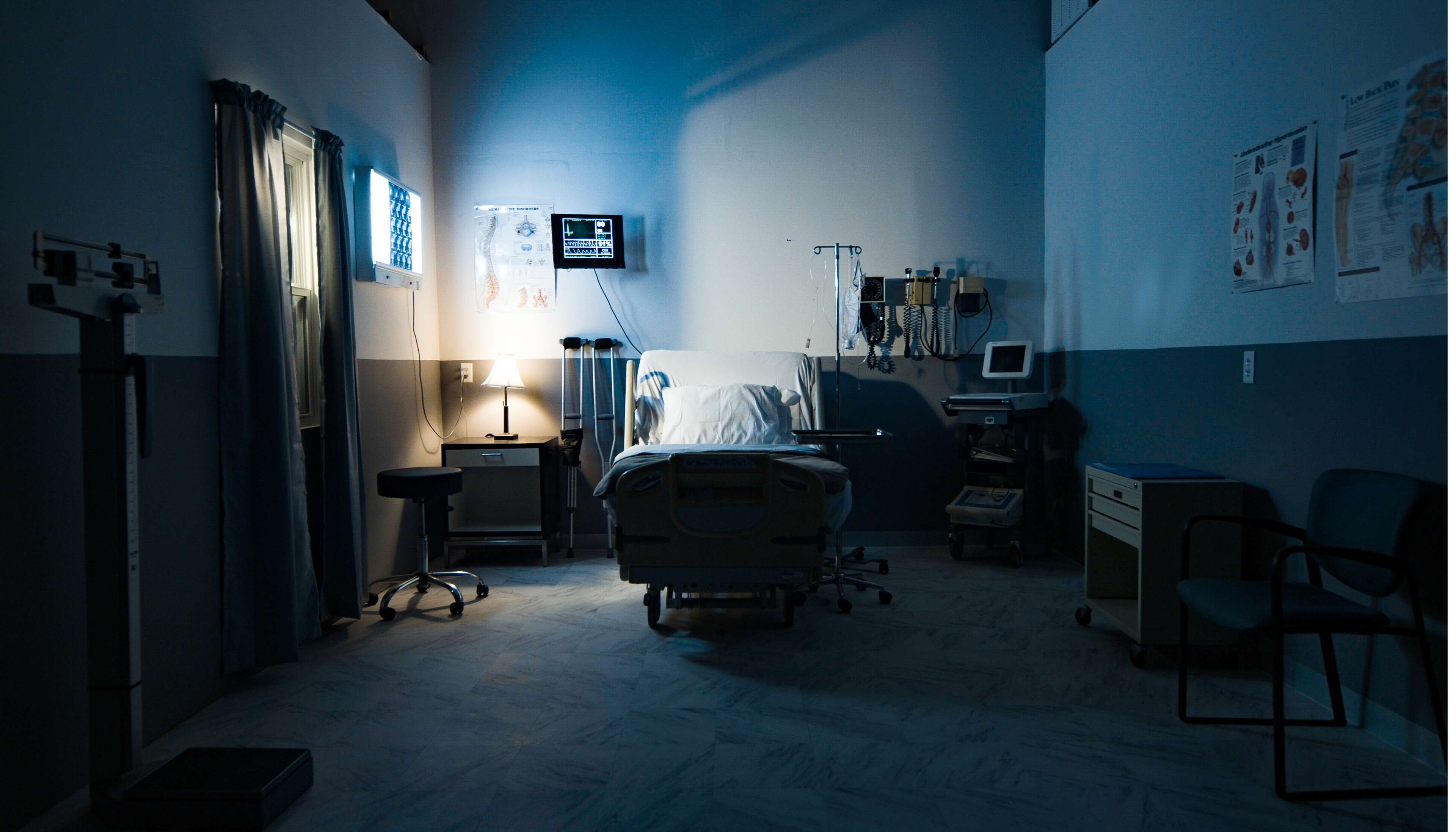 A dimly lit hospital room features a bed, medical equipment, and a monitor displaying vital signs.