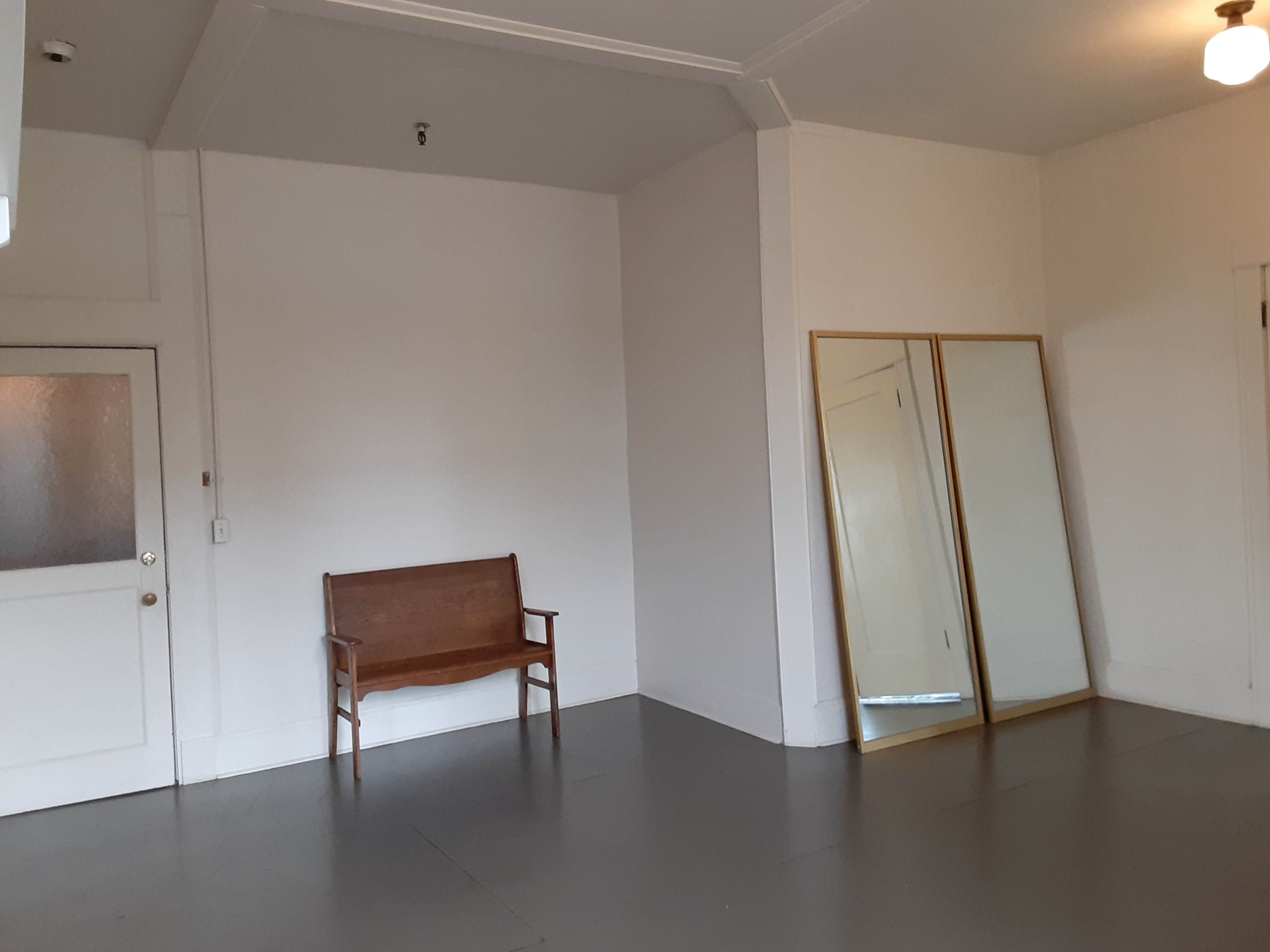 A sparsely furnished room with a wooden bench and two large mirrors against a wall.