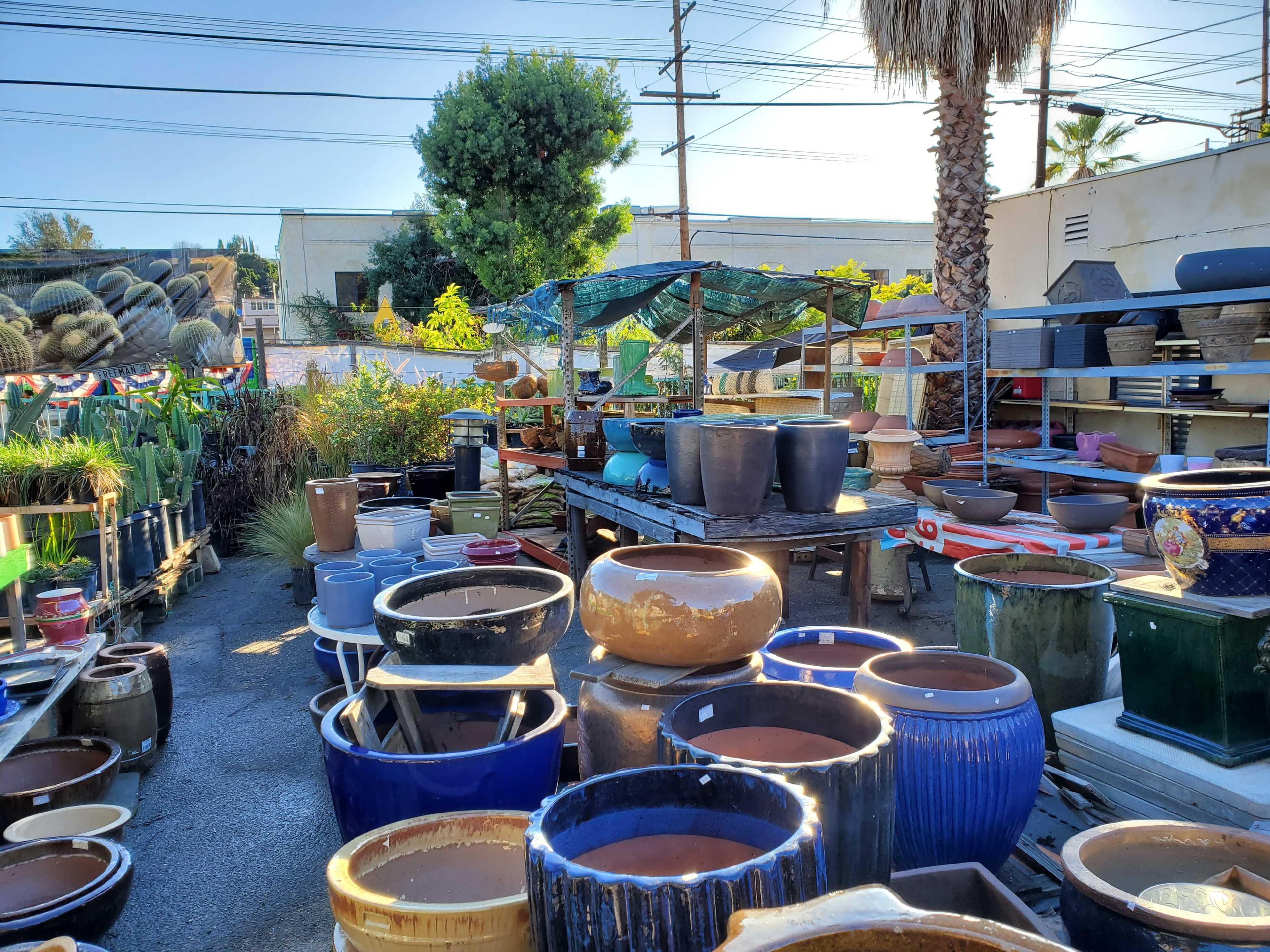 An outdoor garden center filled with various decorative pots and planters displayed on tables and the ground among greenery and trees.
