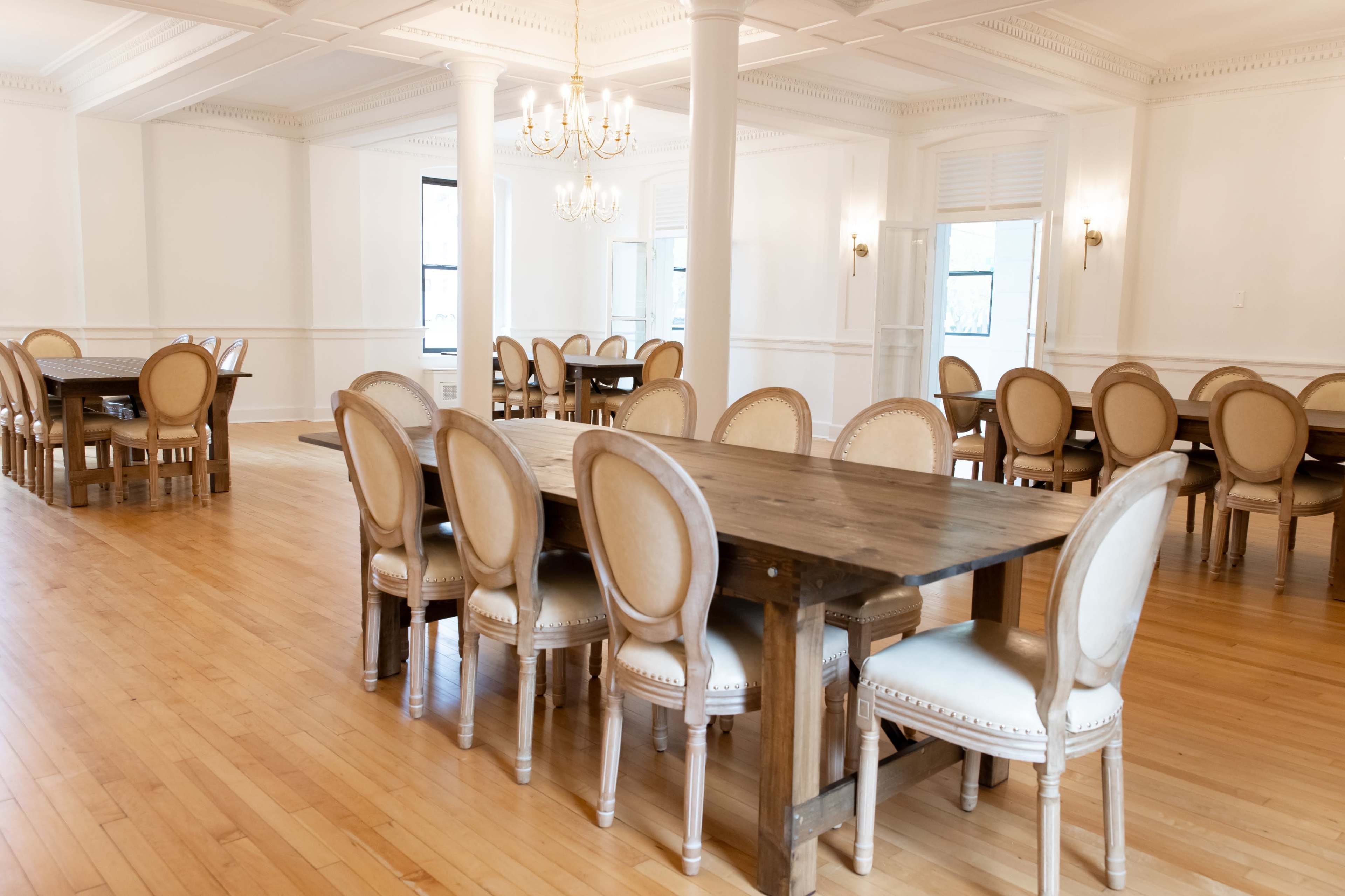A spacious, well-lit dining area with multiple wooden tables surrounded by chairs, all set on a light wooden floor.