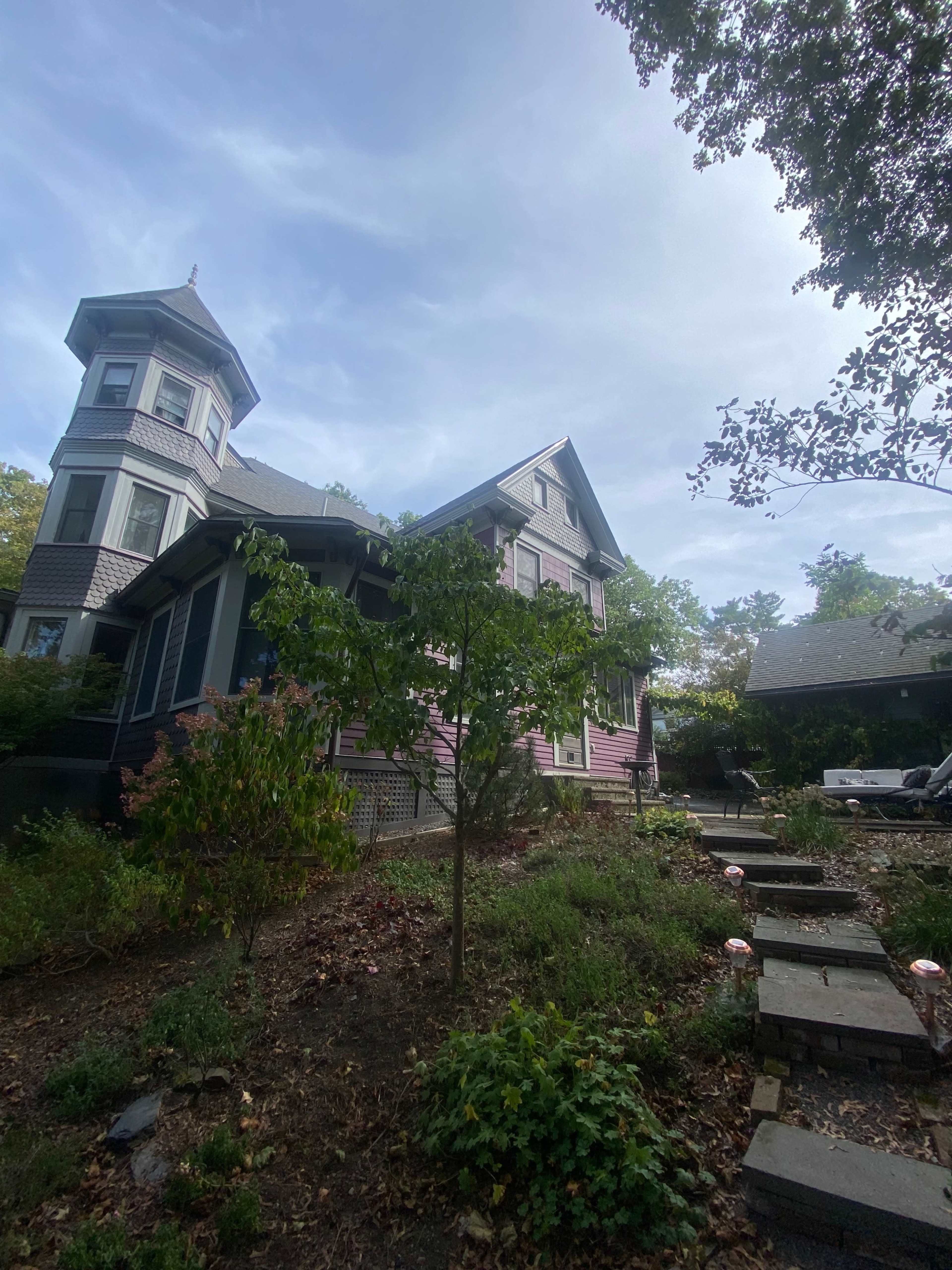 A Victorian-style house with a tower is surrounded by a landscaped garden and stone pathway.