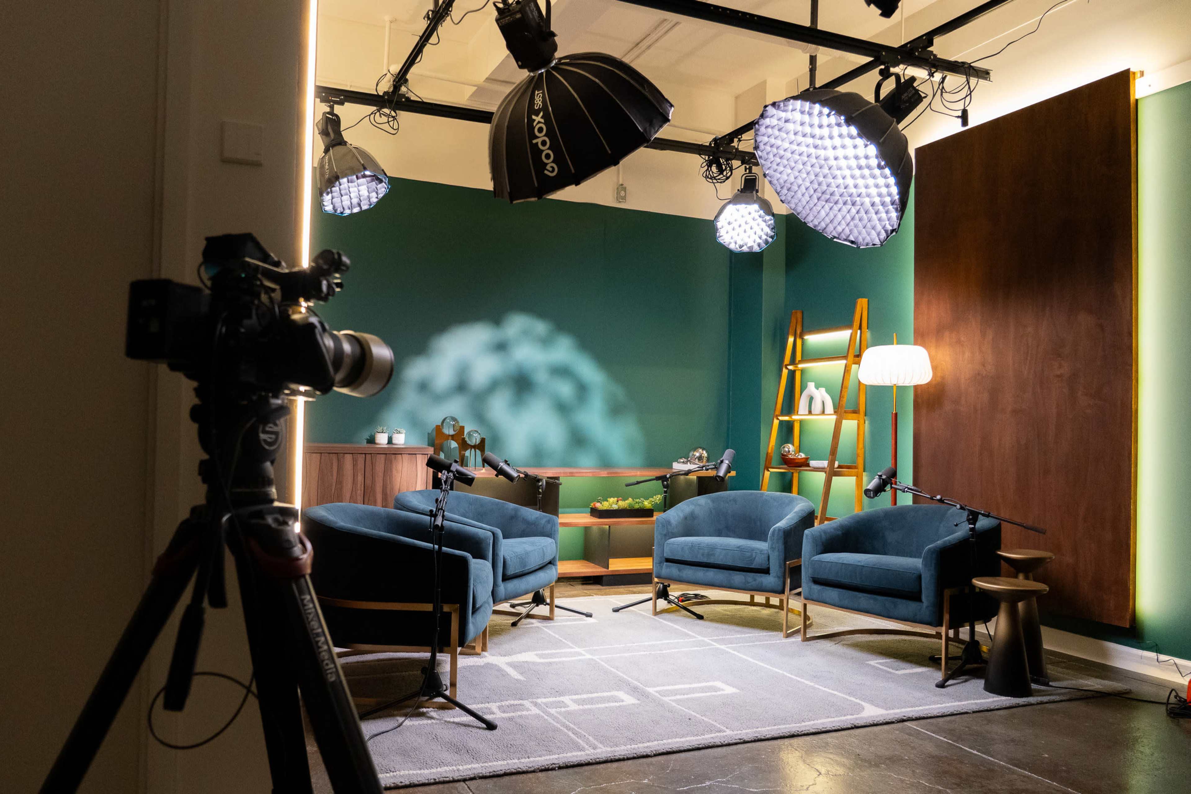 A photography setup features three blue armchairs arranged in a well-lit studio space equipped with studio lights and a camera on a tripod.
