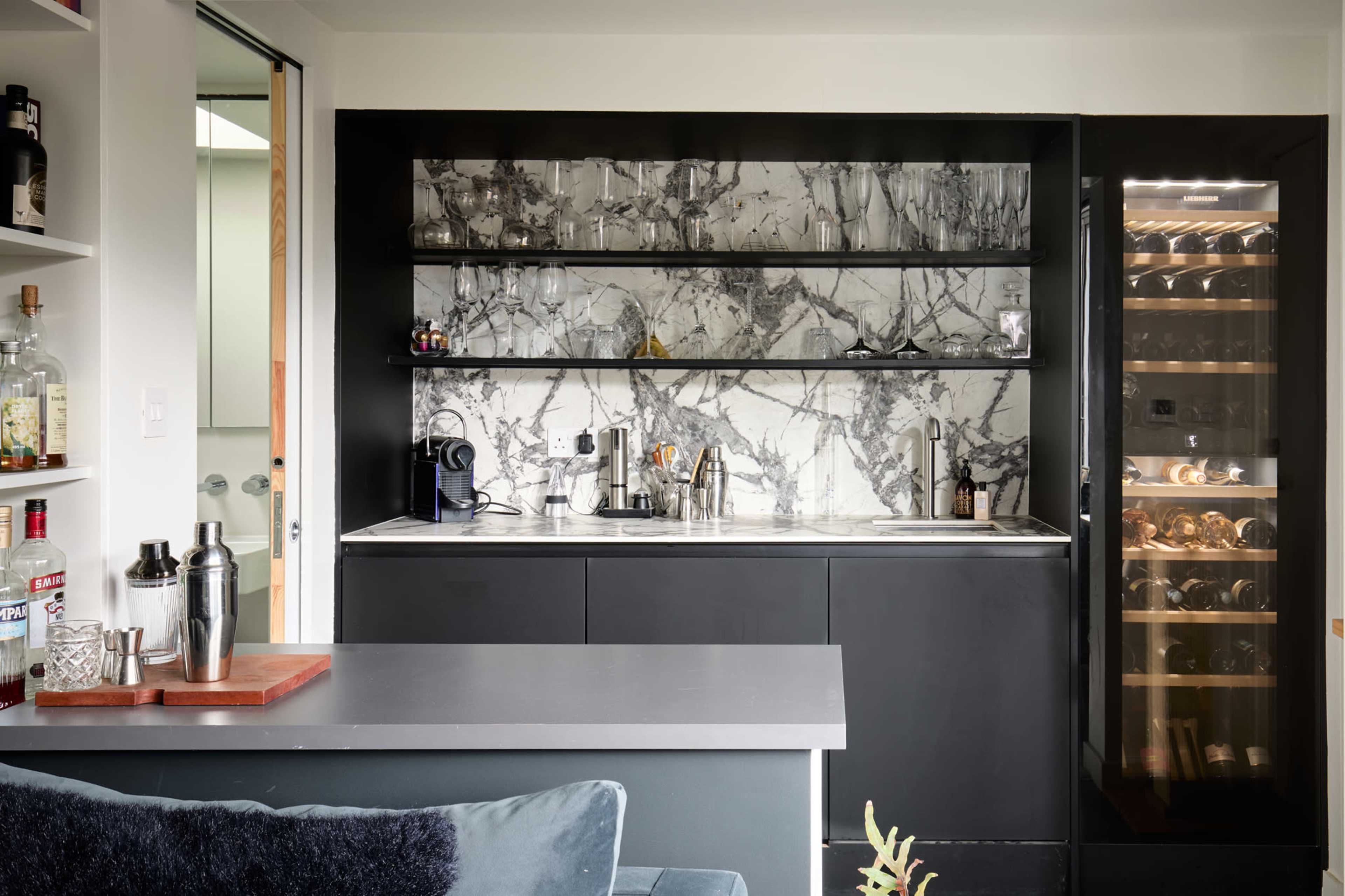 A modern kitchen features a black cabinetry design with marble-patterned backsplash and glass wine storage.