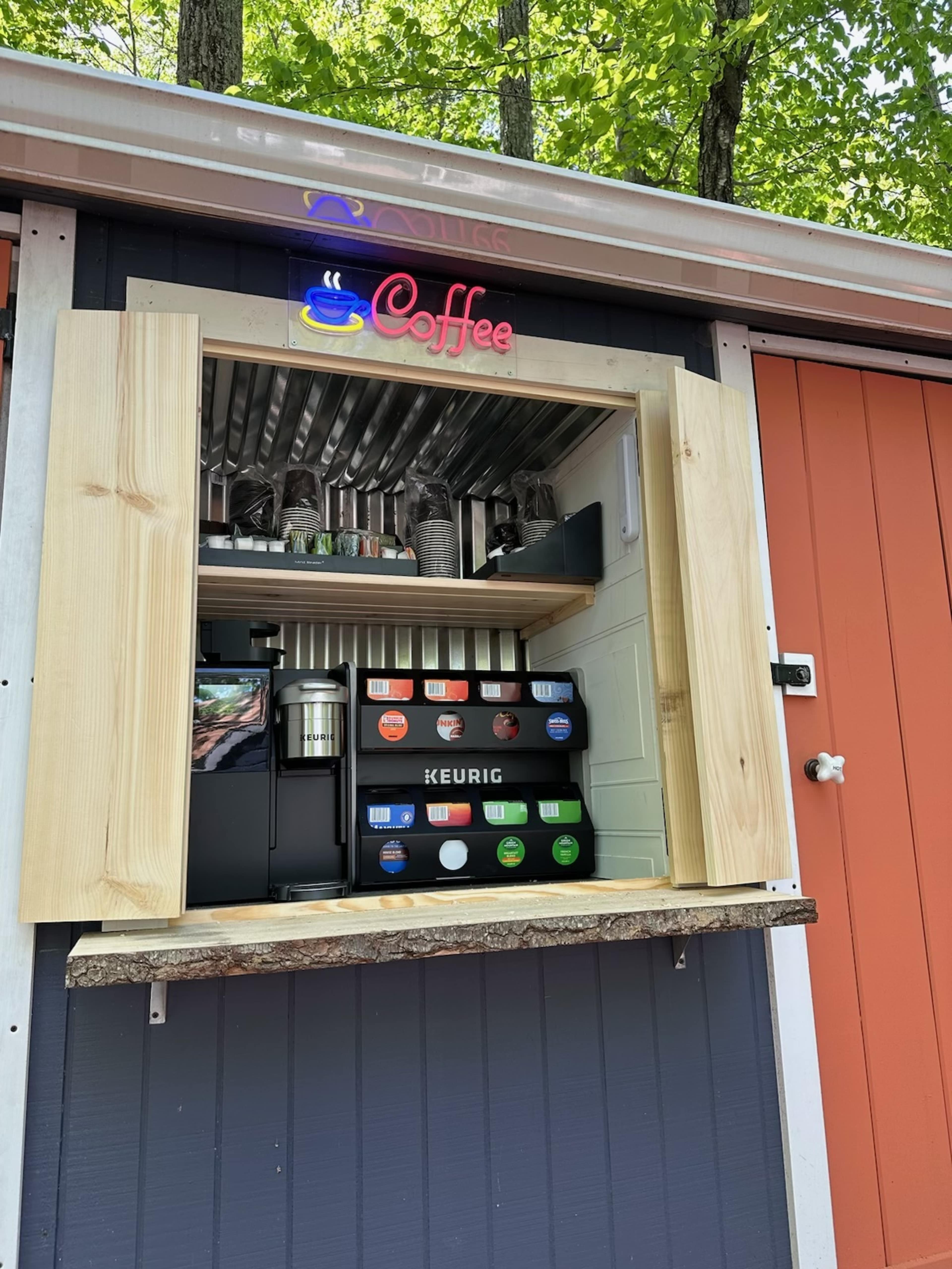 A wooden kiosk features a Keurig coffee machine and various coffee supplies, with a bright "Coffee" sign overhead.