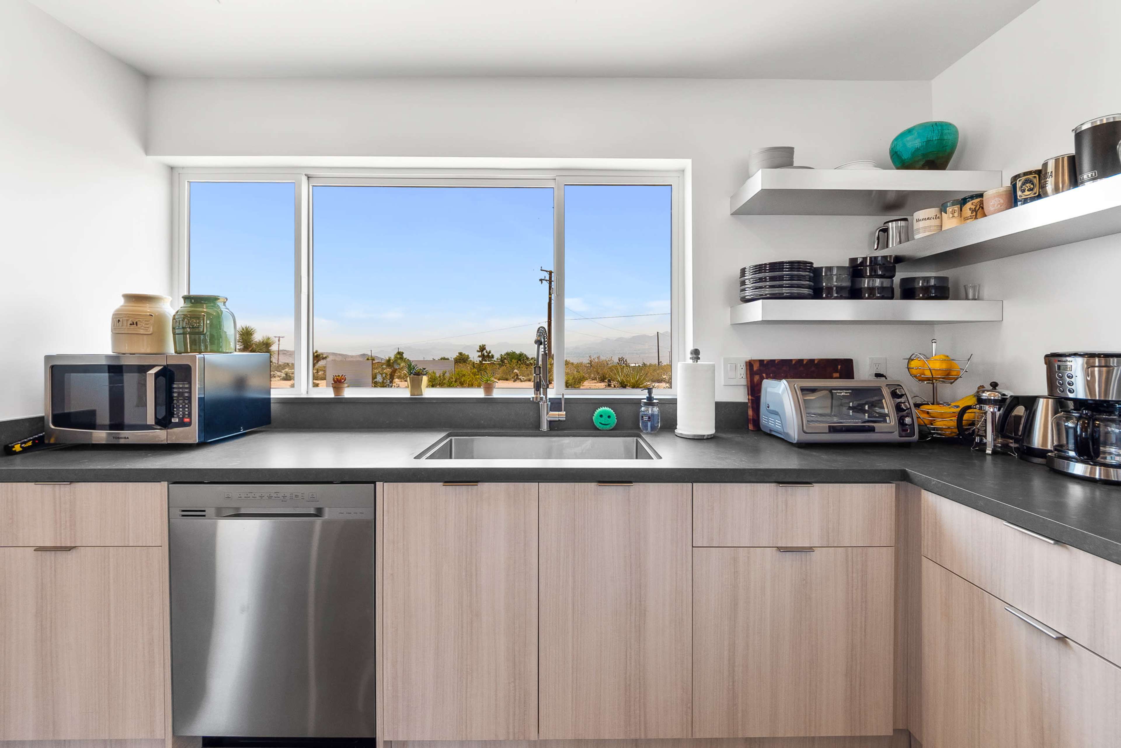 The modern kitchen features a stainless steel dishwasher, a microwave, and a toaster next to a window with a view of the outdoors.