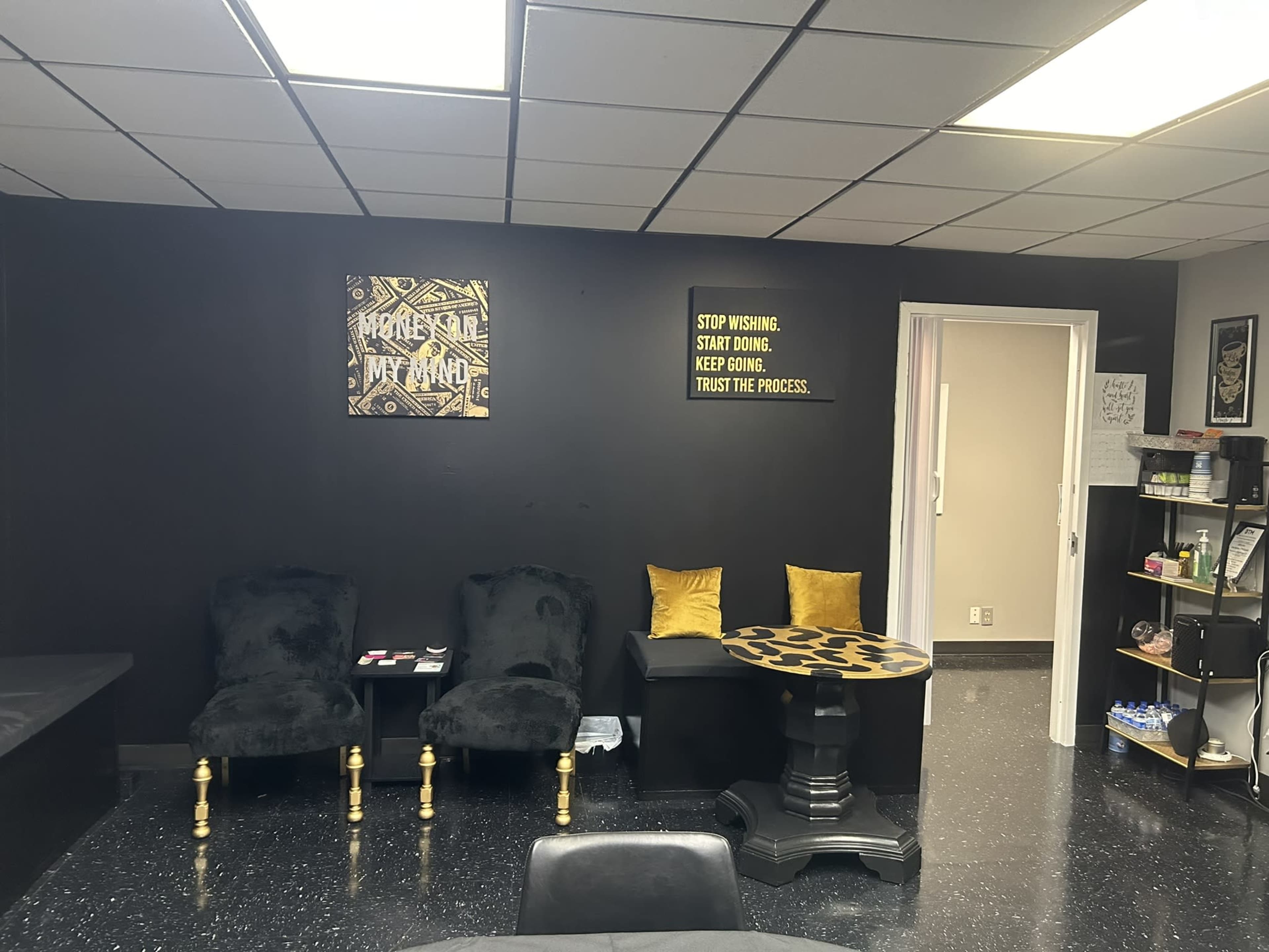 A black-walled room featuring two black chairs, a leopard-print table, and motivational quotes on the wall.