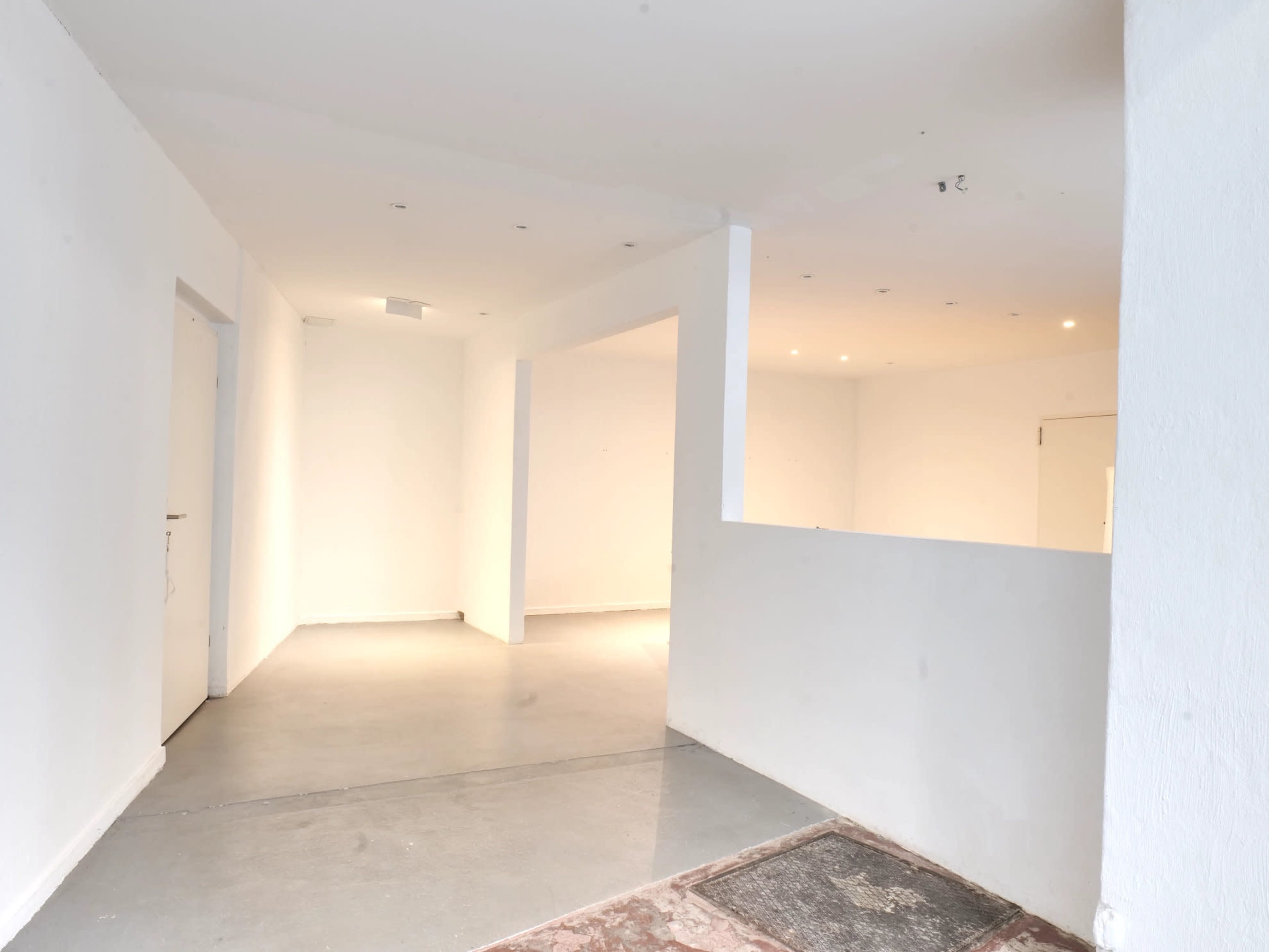The image shows a bare, empty interior space with white walls and a smooth concrete floor.