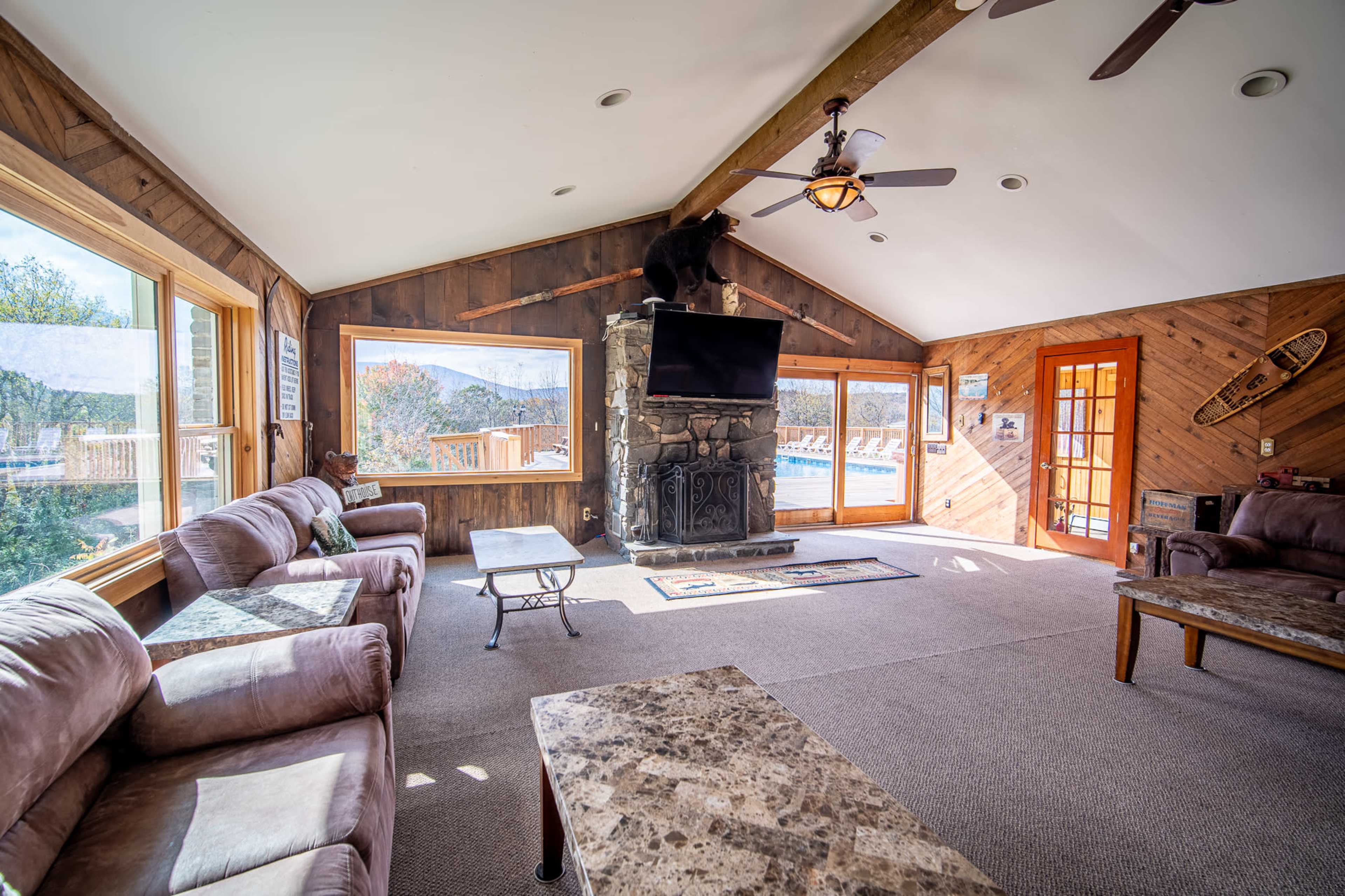 A spacious living room features large windows, a stone fireplace, and comfortable seating arrangements.