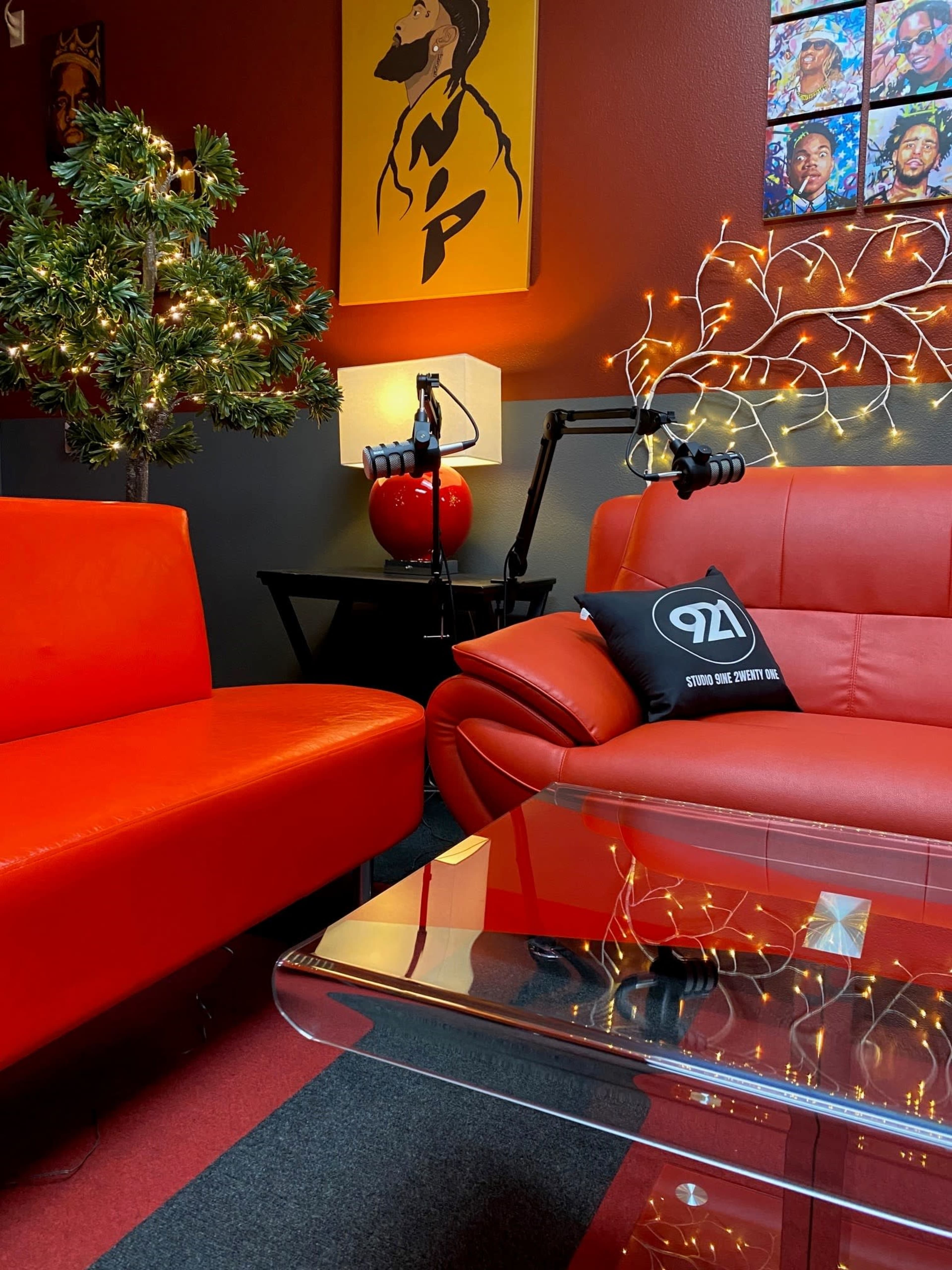 The scene features a cozy lounge area with two red sofas, a glass coffee table, a small tree adorned with lights, and artistic wall decor.