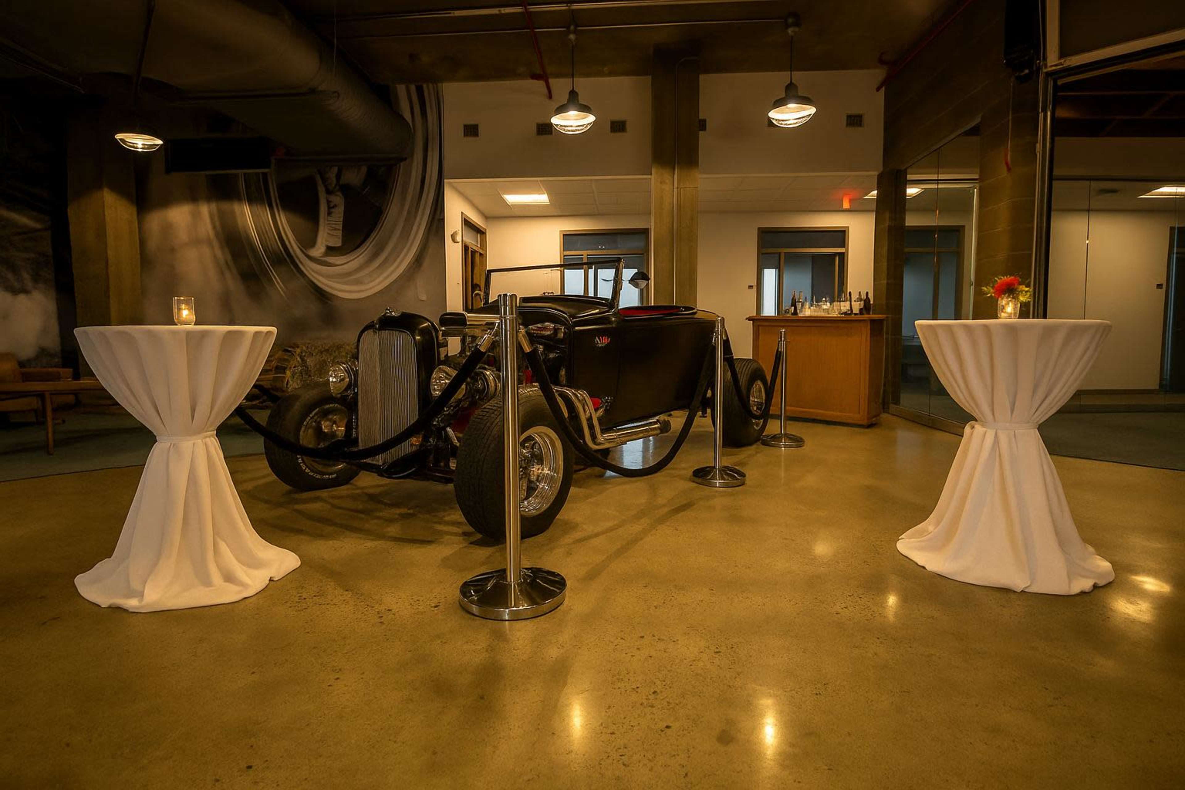 A vintage car is displayed in a spacious room with two elegantly draped tables on either side.