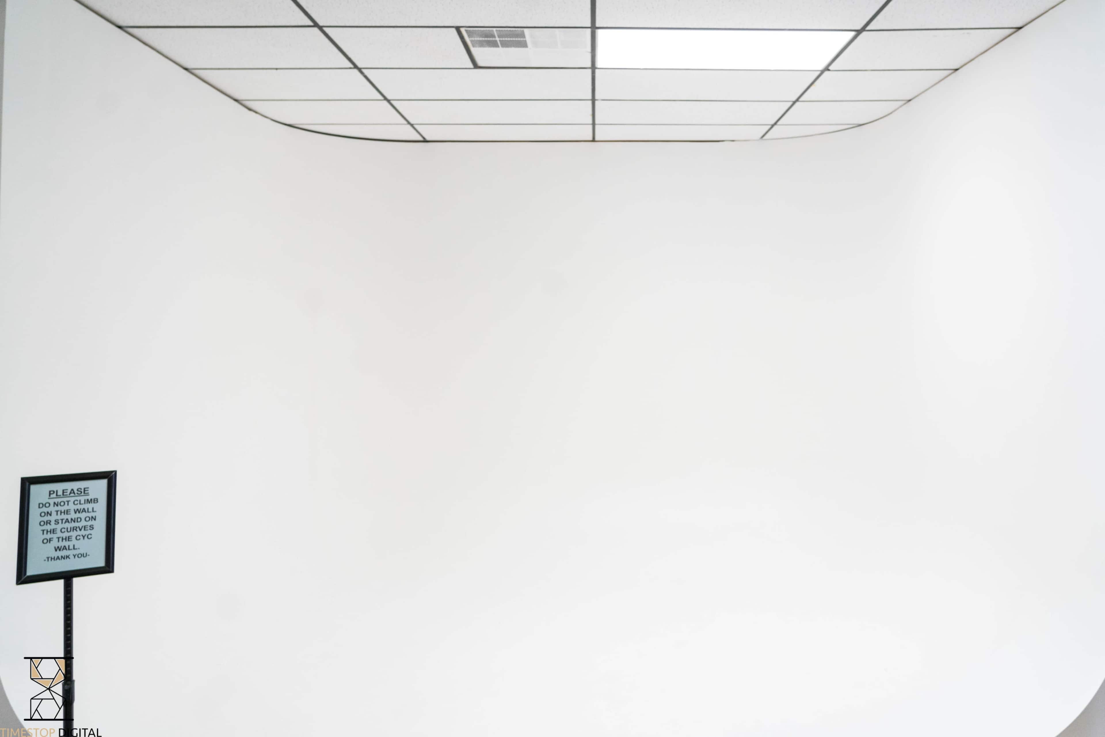 The image shows a blank white room with a smooth curved wall and a sign on the left side.