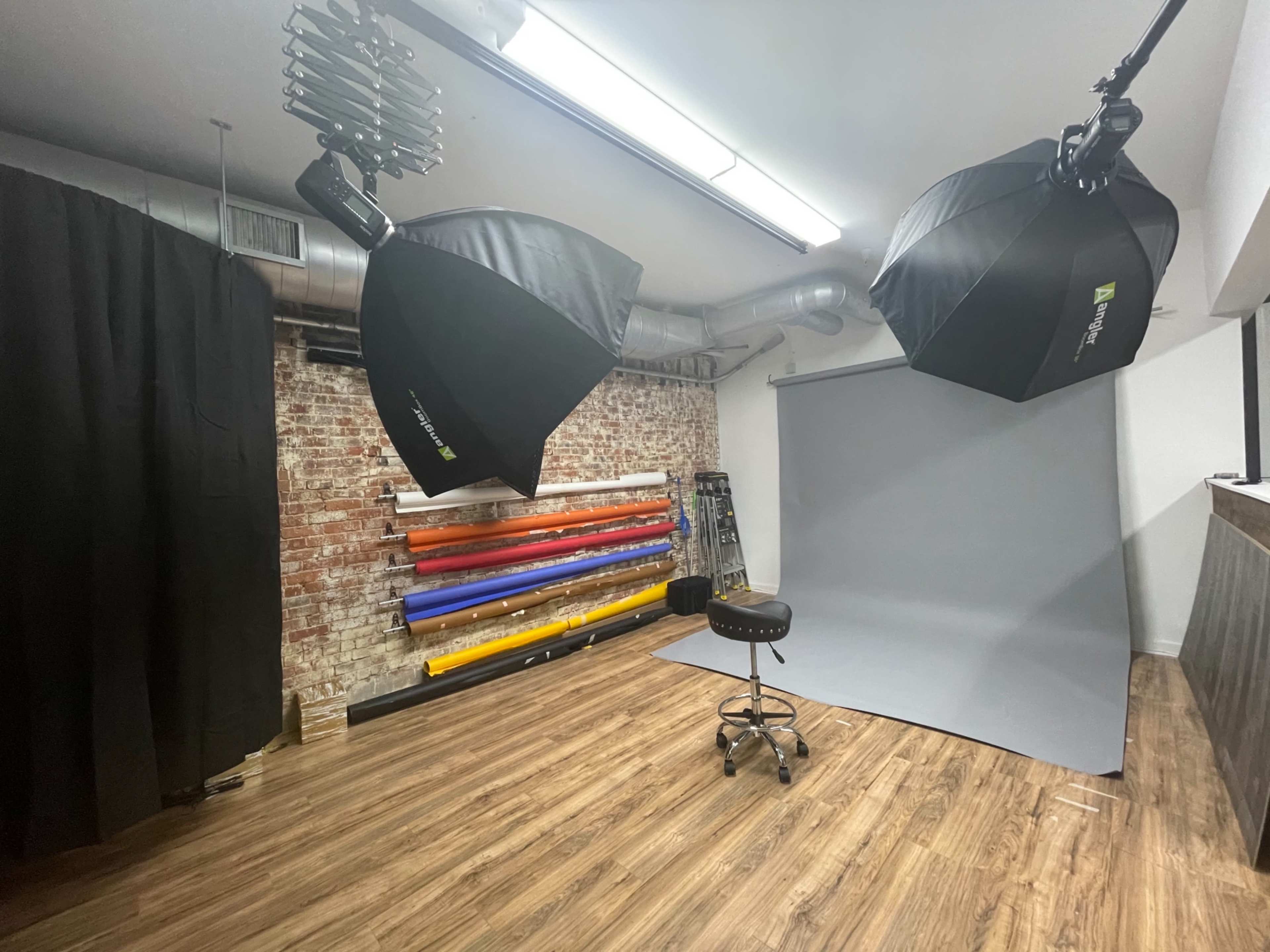 A photography studio equipped with two large softbox lights, a gray backdrop, and a selection of colored backdrops neatly arranged on a wall.